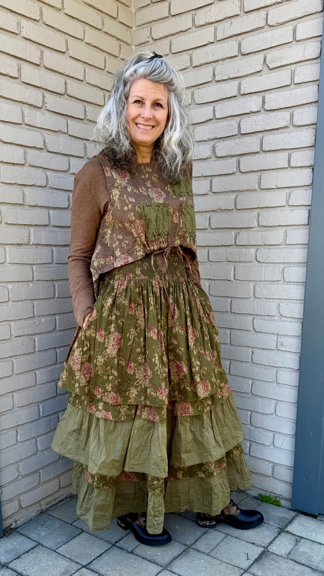 Woman in a layered, vintage-style outfit standing against a brick wall.