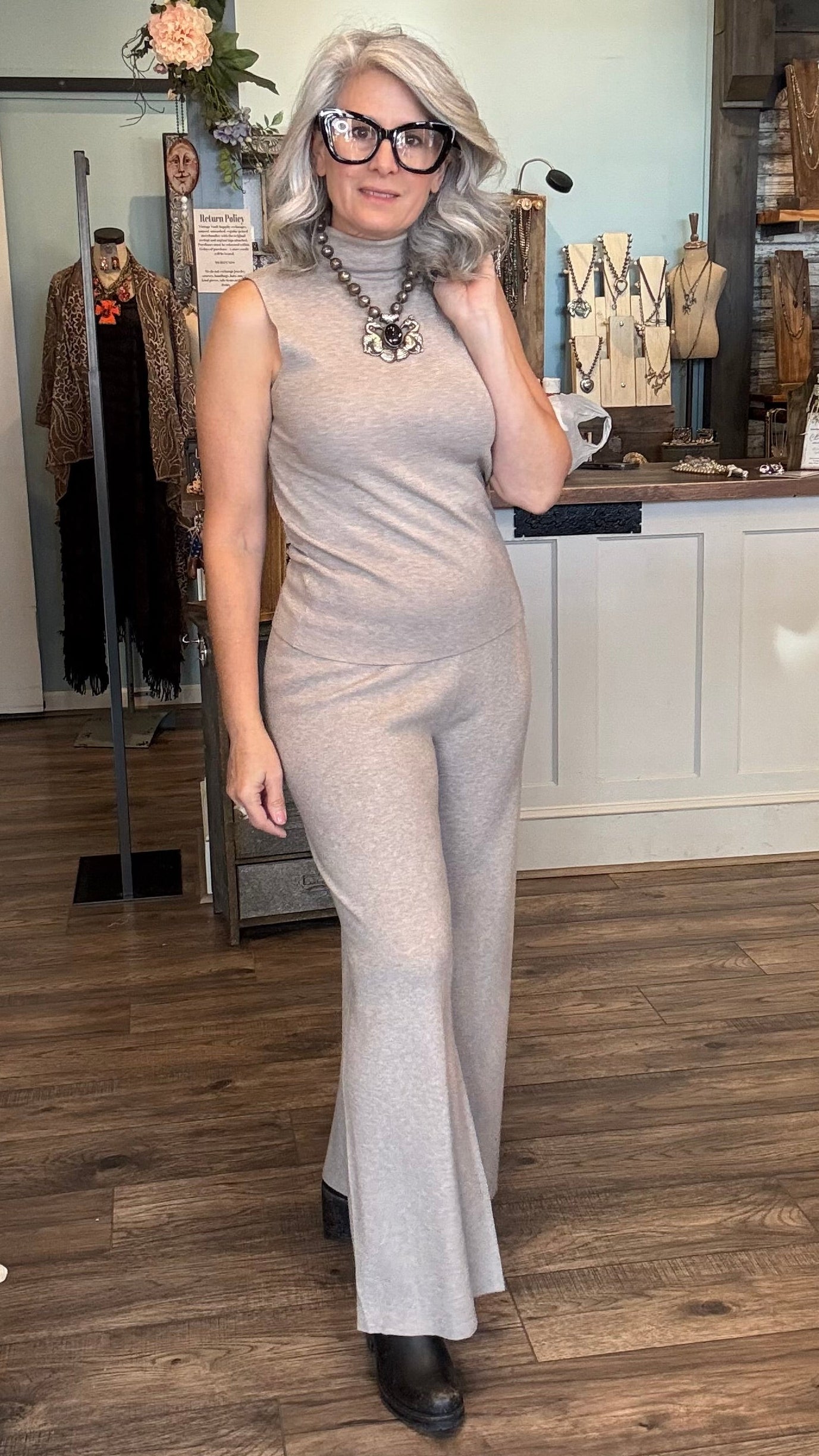 Woman in a khaki sweater pant set posing in a room with wooden flooring and a counter.