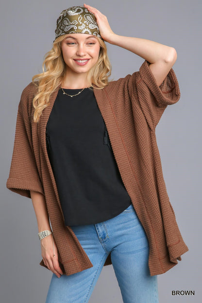 Woman wearing a brown cardigan, black top, and blue jeans on a gray background