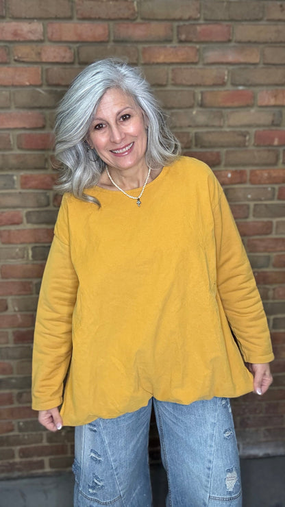Woman wearing the Solid Mustard Puckered Pullover  and the Upside Down Jeans standing in front of a brick wall.