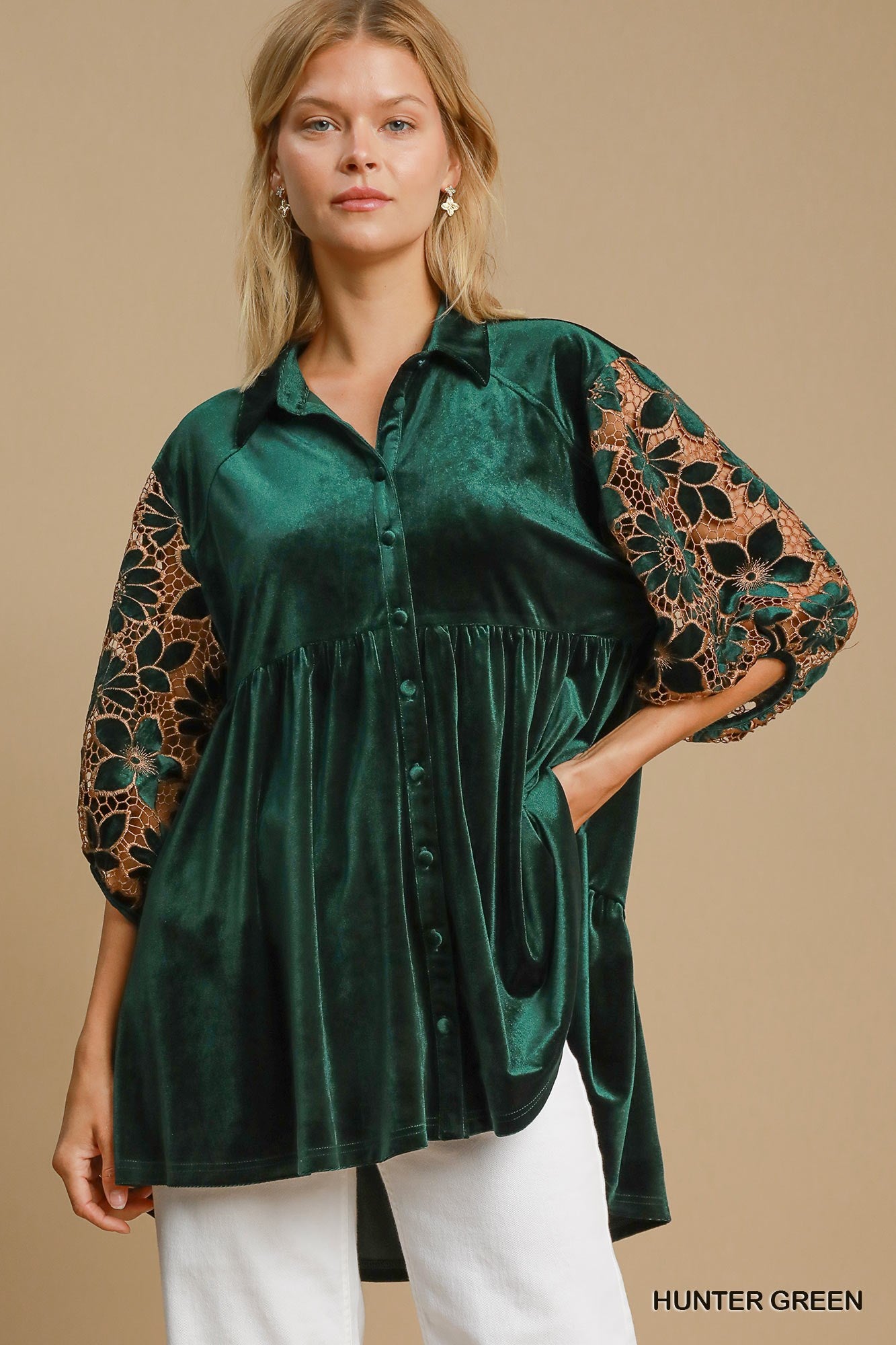 Woman wearing a green velvet blouse with lace sleeves on a beige background