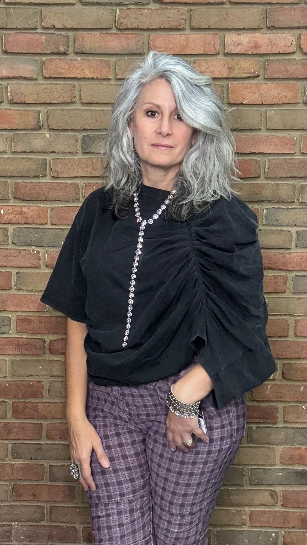 Person wearing a black top and plaid pants against a brick wall
