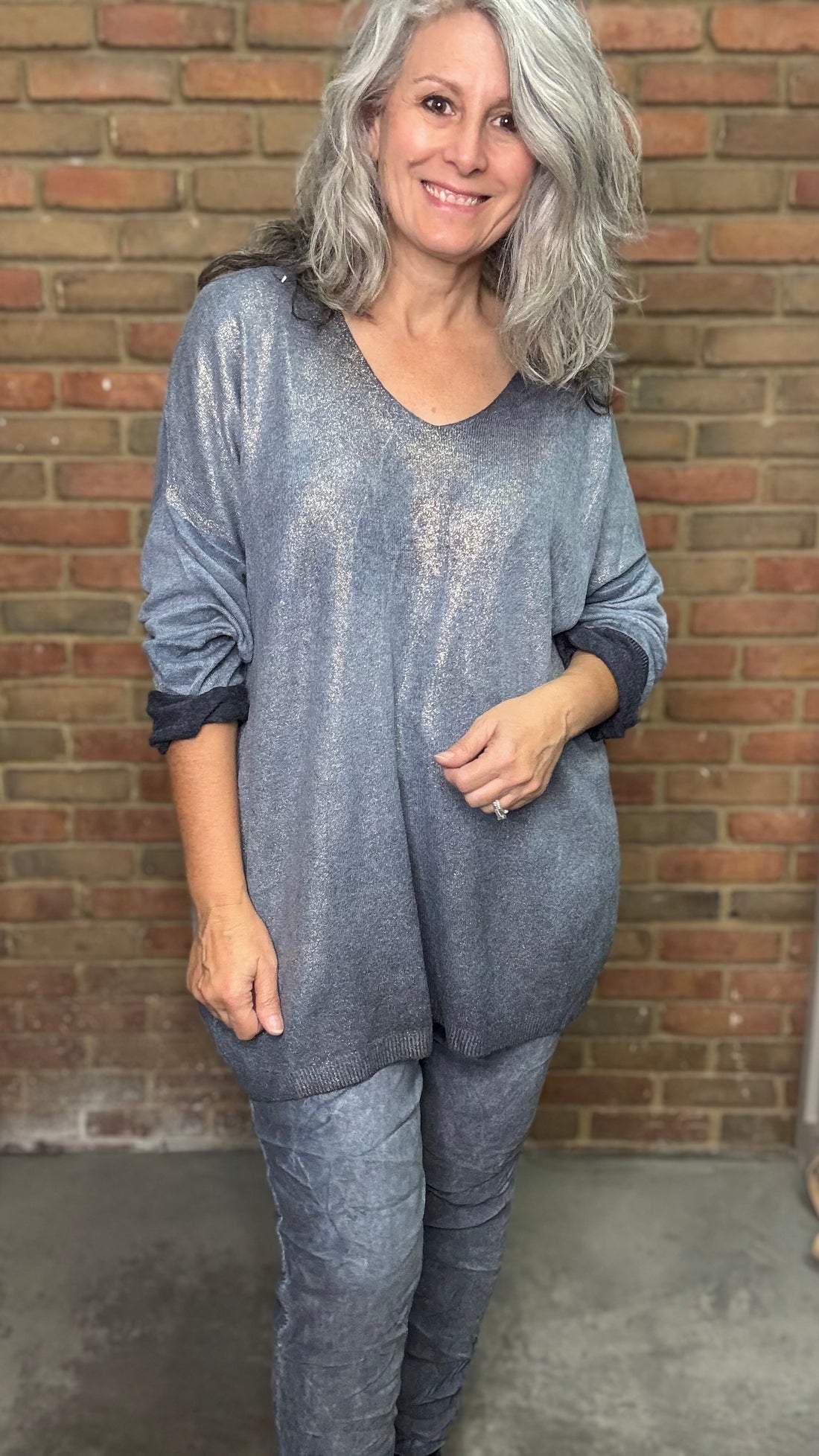 Woman wearing a blue outfit standing against a brick wall.