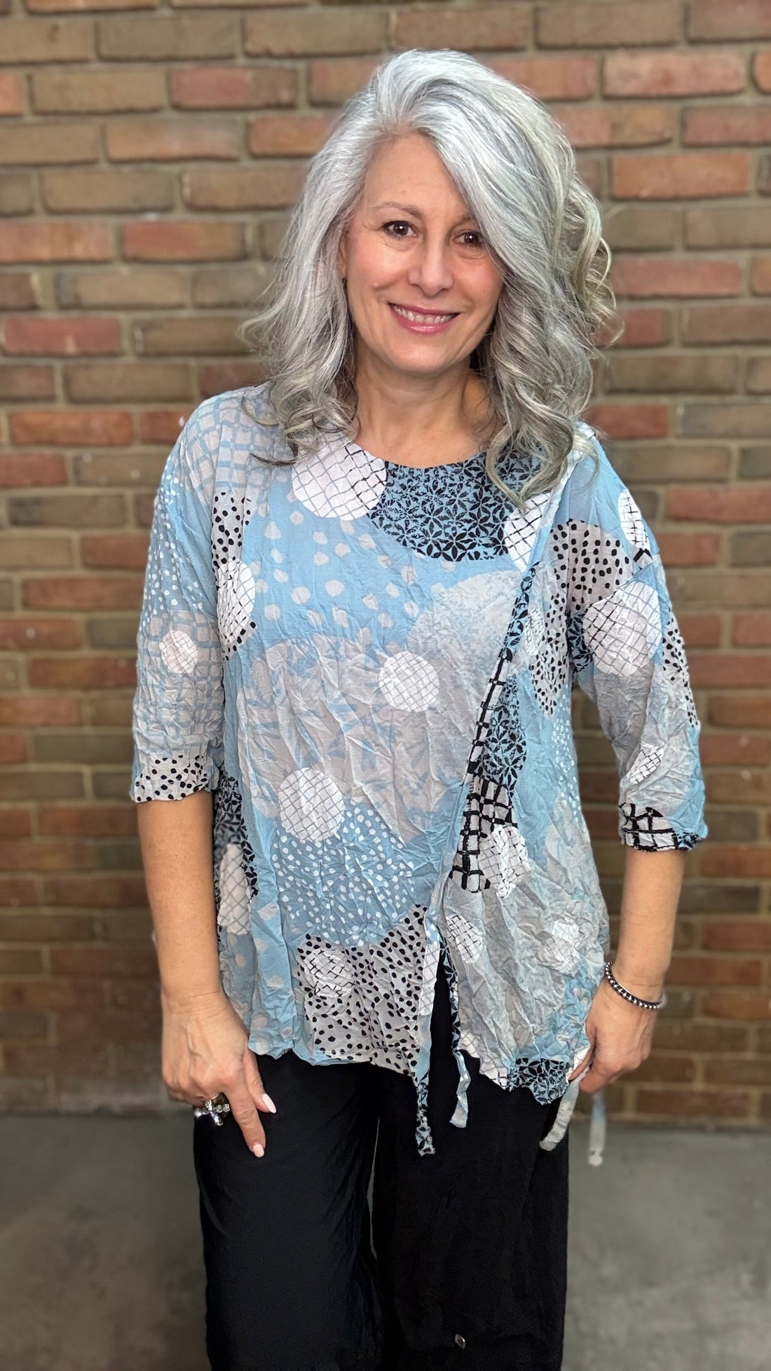 Woman wearing Laurie Top - Sky against a brick wall.