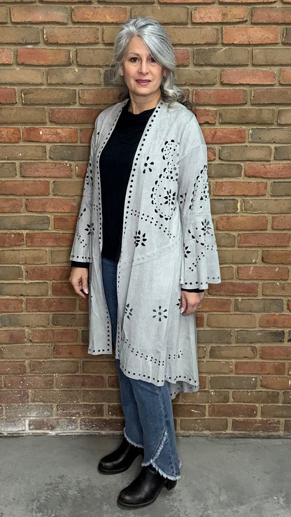 Woman wearing the Grey Suede Laser Cut Jacket standing against a brick wall.