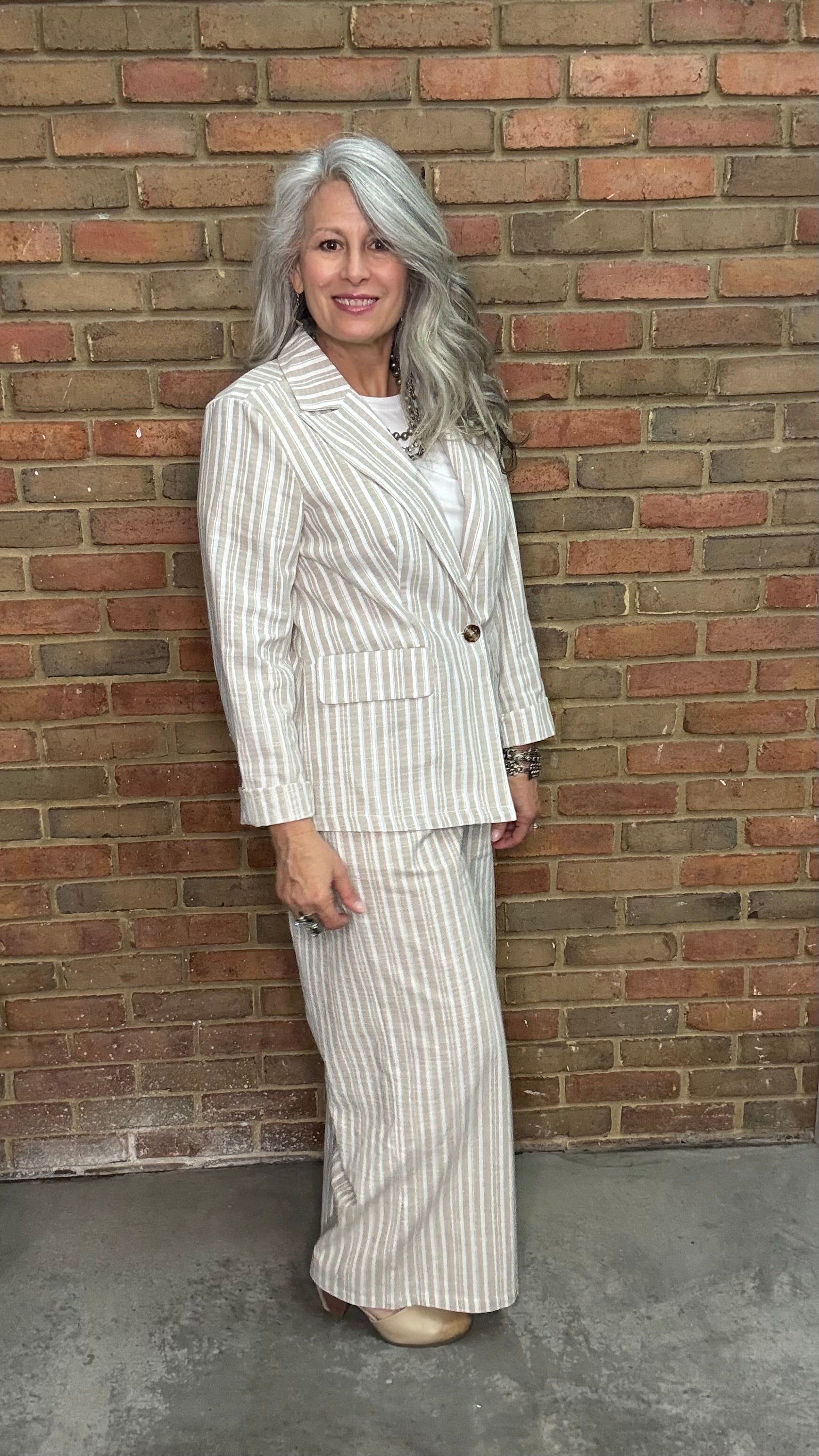 Woman wearing a Linen Stripped Blazer and Linen Stripe Pant standing against a brick wall.