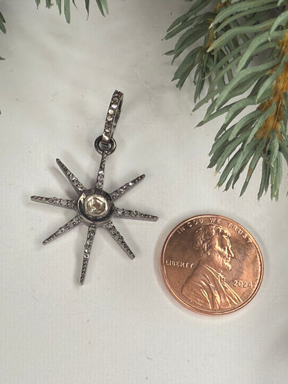 Star-shaped silver pendant with a central gemstone next to a penny on a light background with greenery.