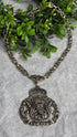 Decorative necklace with intricate design on a textured surface with greenery