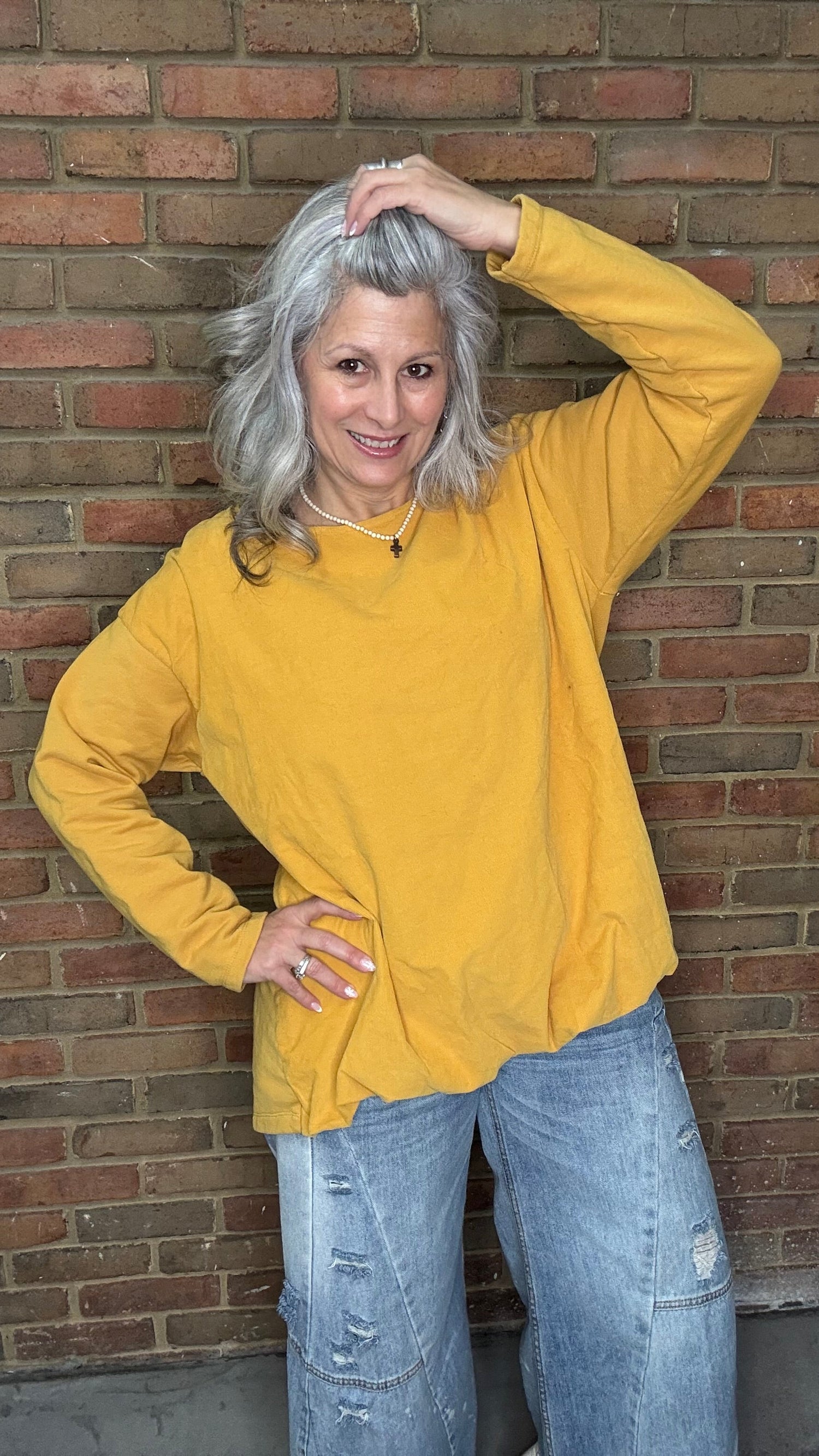 Woman wearing the Solid Mustard Puckered Pullover  and the Upside Down Jeans standing in front of a brick wall.
