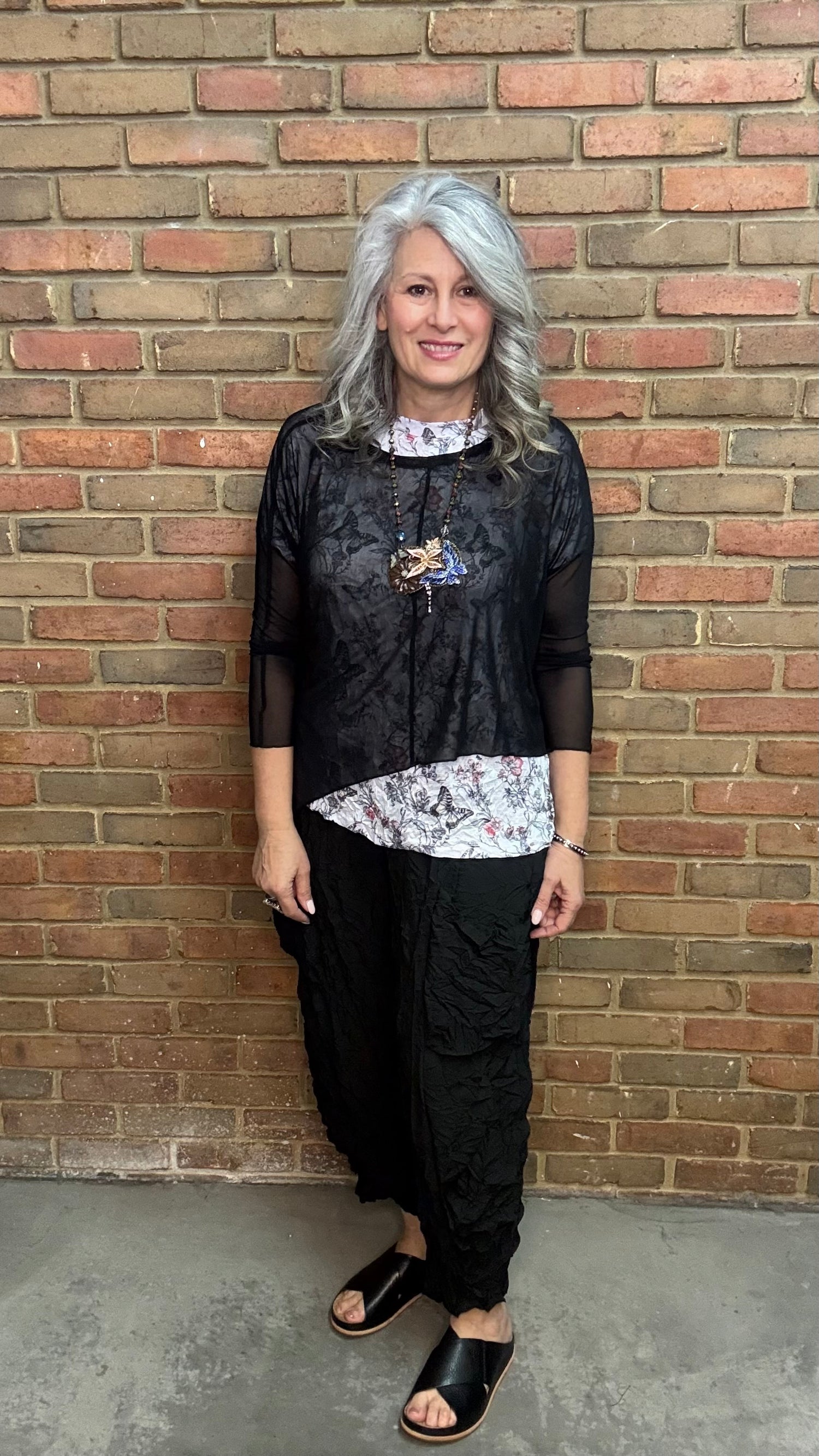 Woman standing against Solid Mesh Topper Black and black pants.