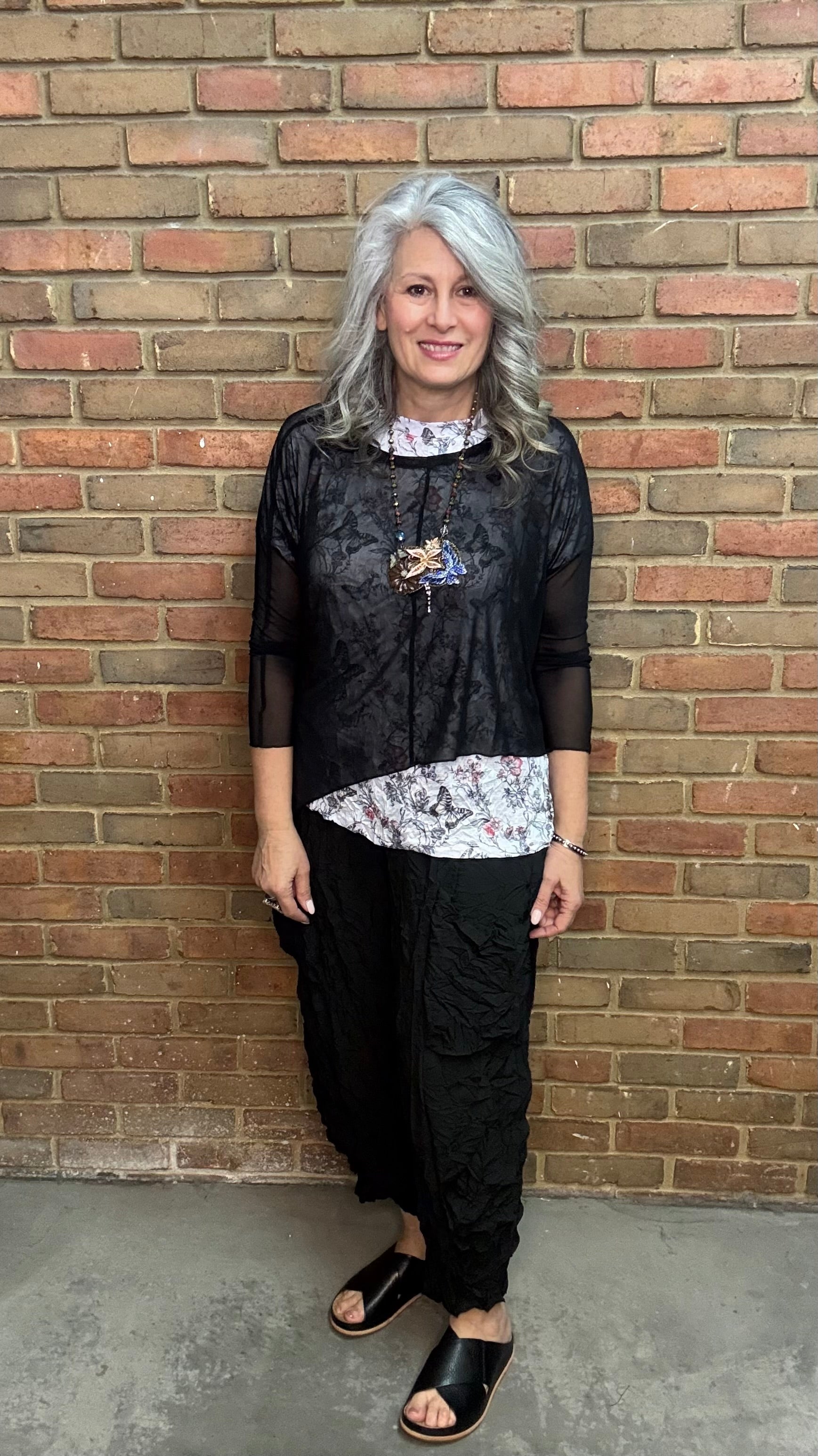 Woman standing against Solid Mesh Topper Black and black pants.