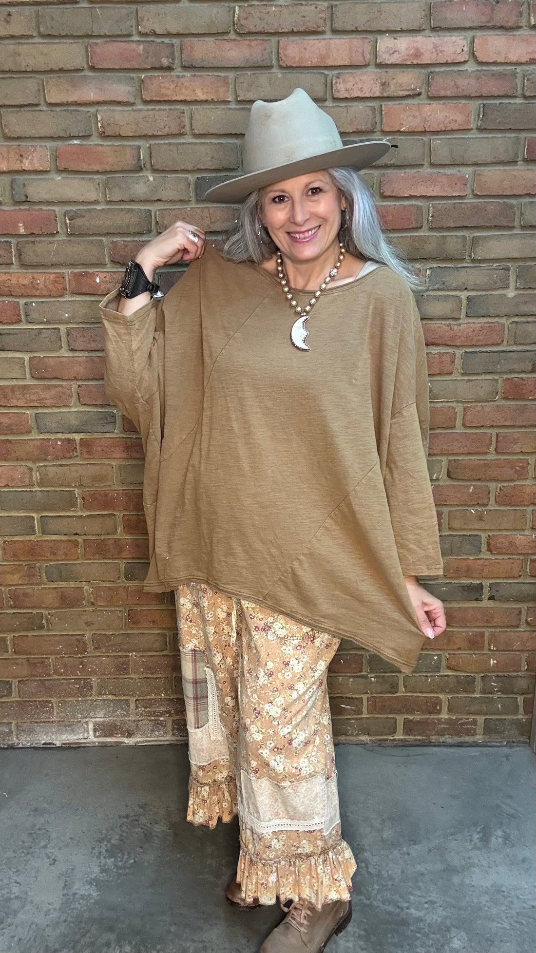 Woman wearing Be Free Top - Vintage Latte and patterned pants against a brick wall.