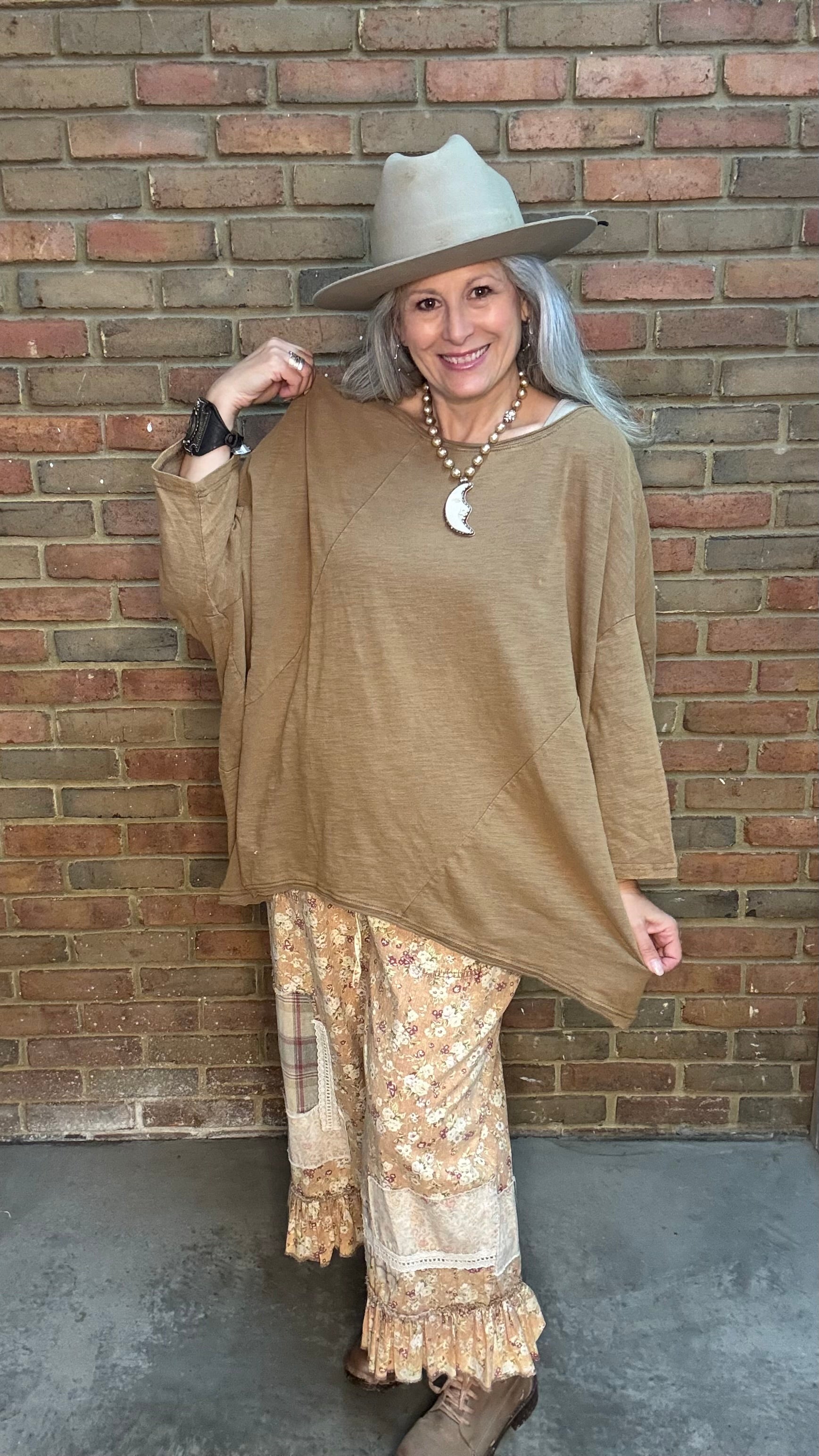 Woman wearing Be Free Top - Vintage Latte and patterned pants against a brick wall.