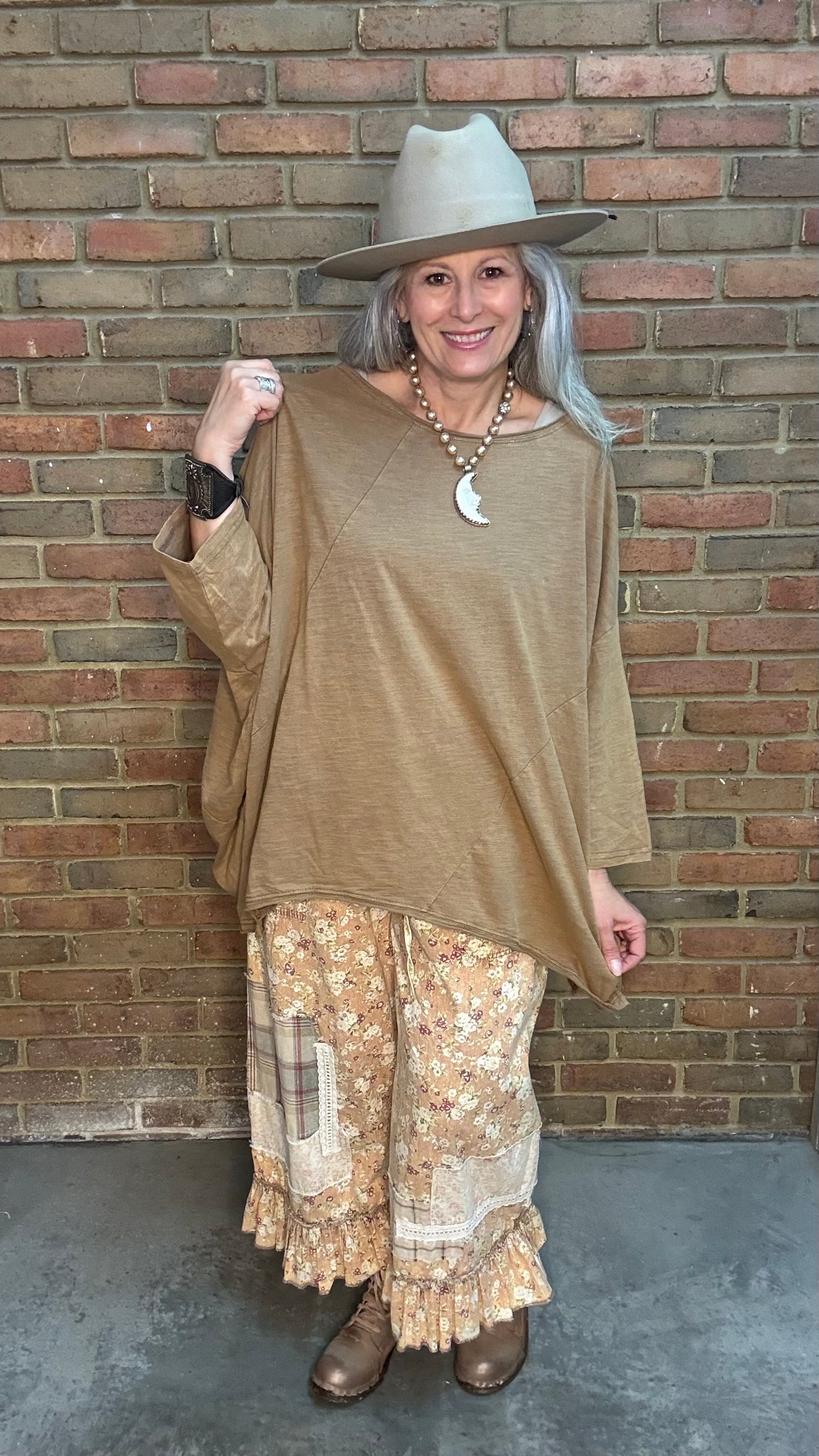 Woman wearing Be Free Top - Vintage Latte and patterned pants against a brick wall.
