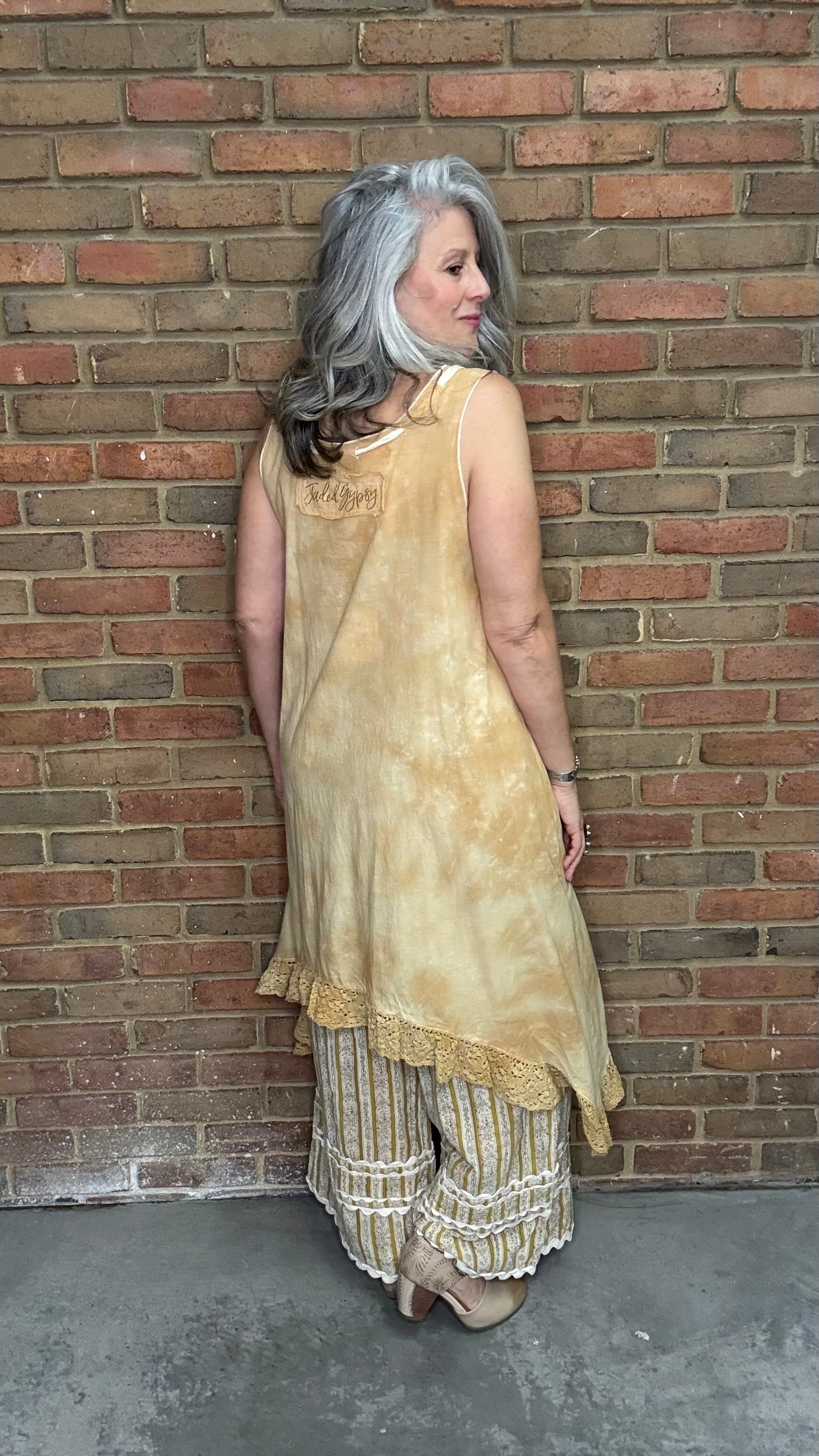 Woman wearing the Wandering Spirit Dress a tea stained tank dress with striped pants standing in front of a brick wall.