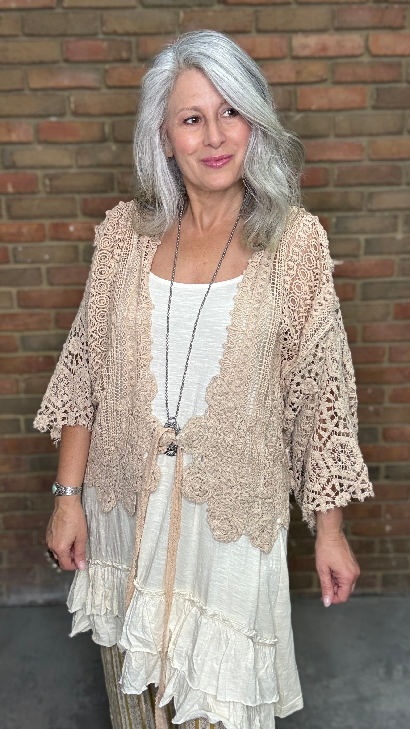 Woman wearing the crochet Forever Timeless Split Tails Jacket over a dress with striped pants standing against a brick wall.