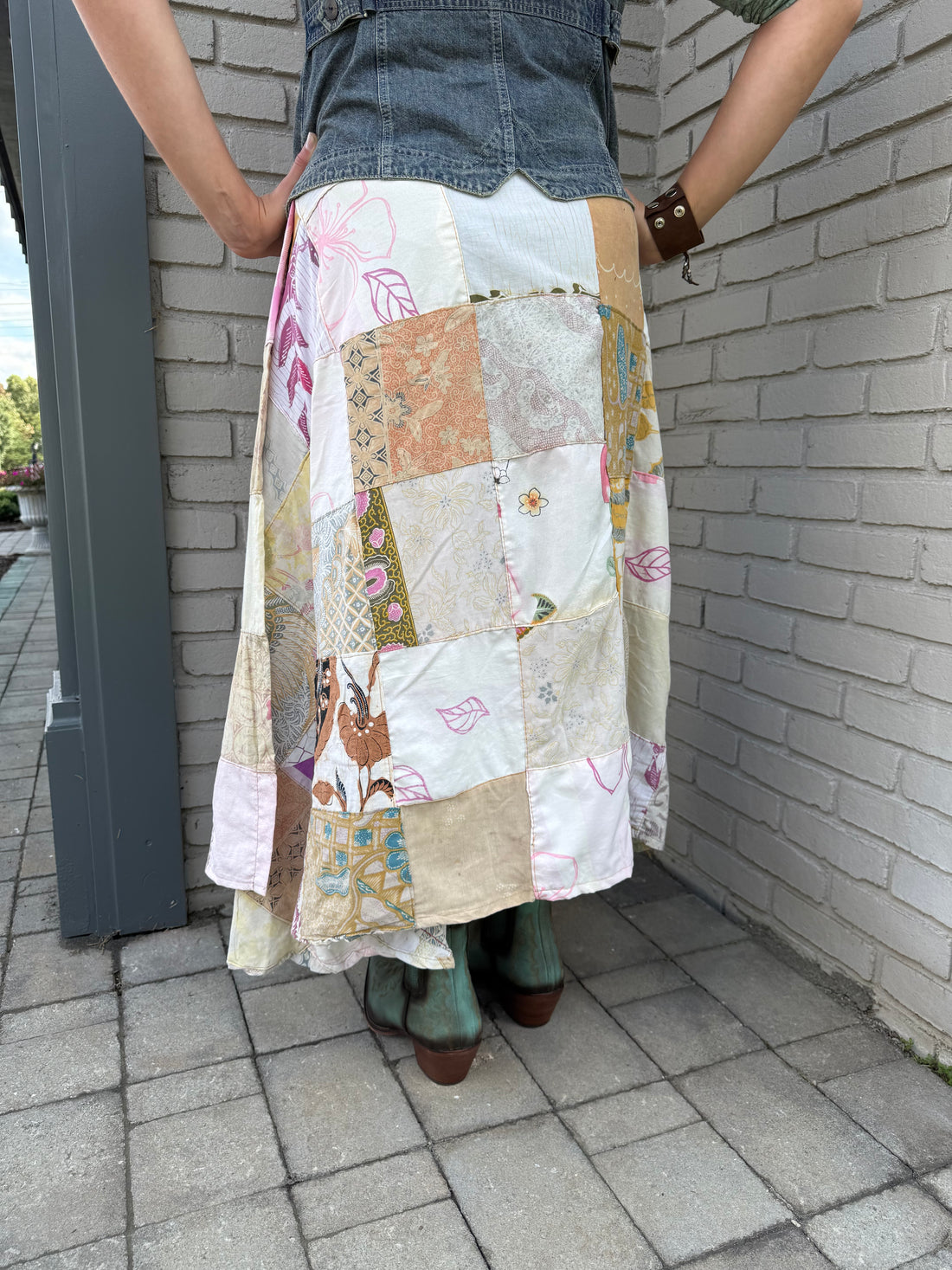 Back of a woman wearing a patchwork skirt standing at the corner of a building.