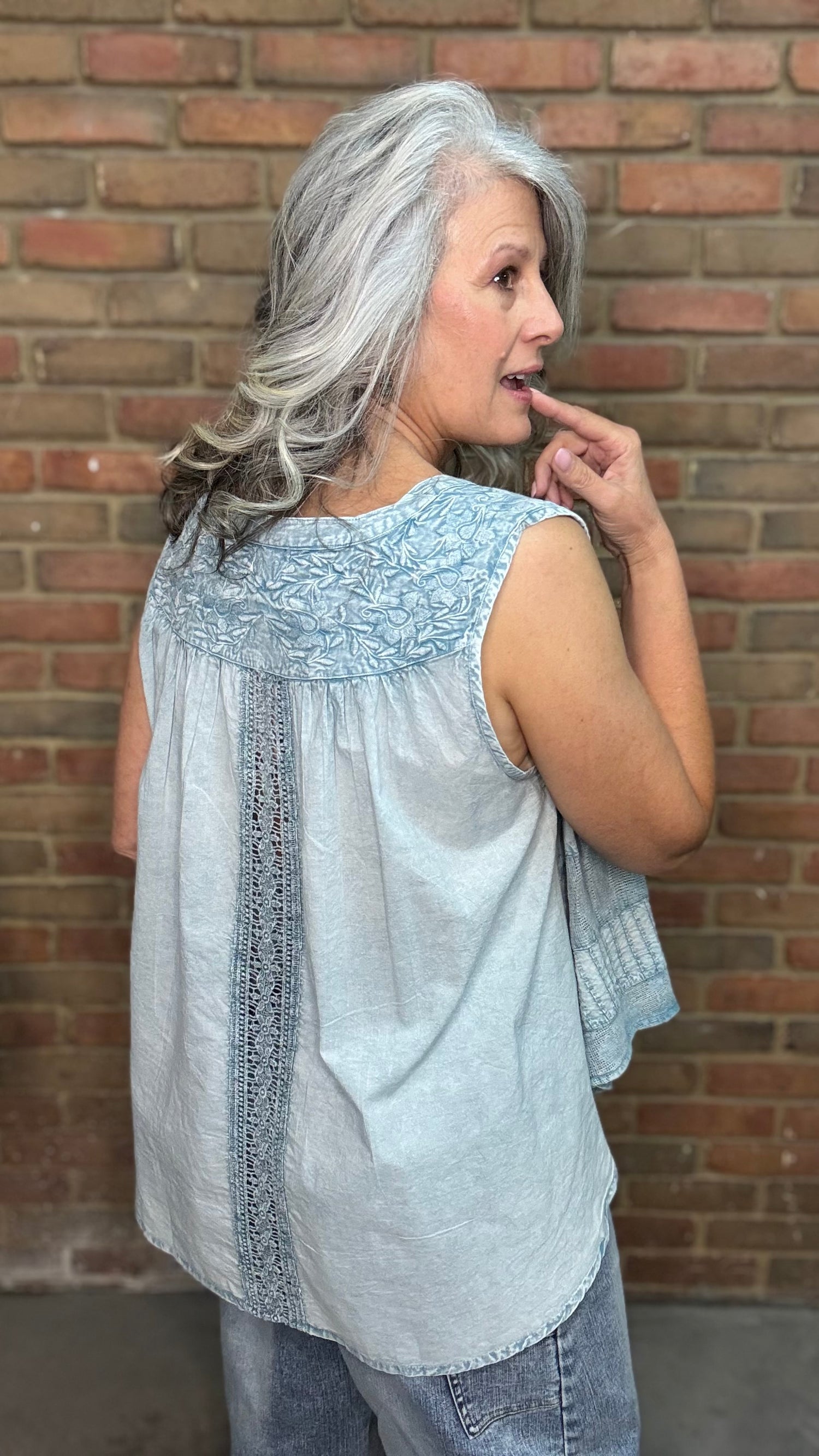 Woman wearing the Denim Blue Crochet Contrast Tank Top, a light blue sleeveless top and jeans standing against a brick wall.