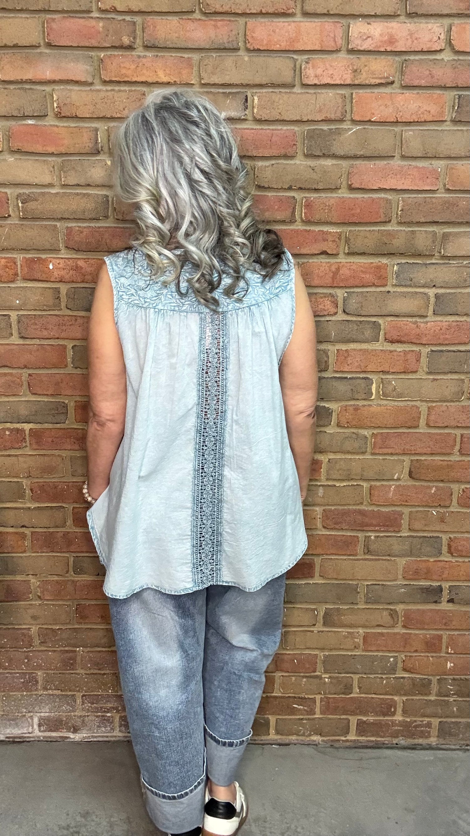 Woman wearing the Denim Blue Crochet Contrast Tank Top, a light blue sleeveless top and jeans standing against a brick wall.