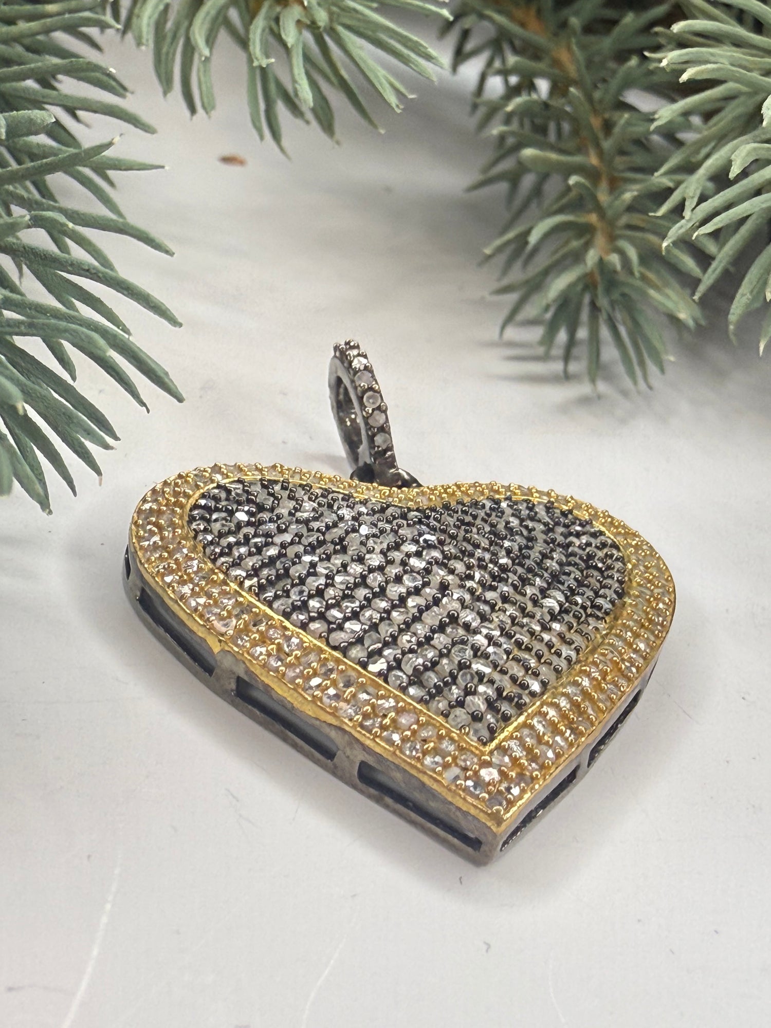 Heart shaped gold and silver pendant with pave diamonds on a white background with greenery.