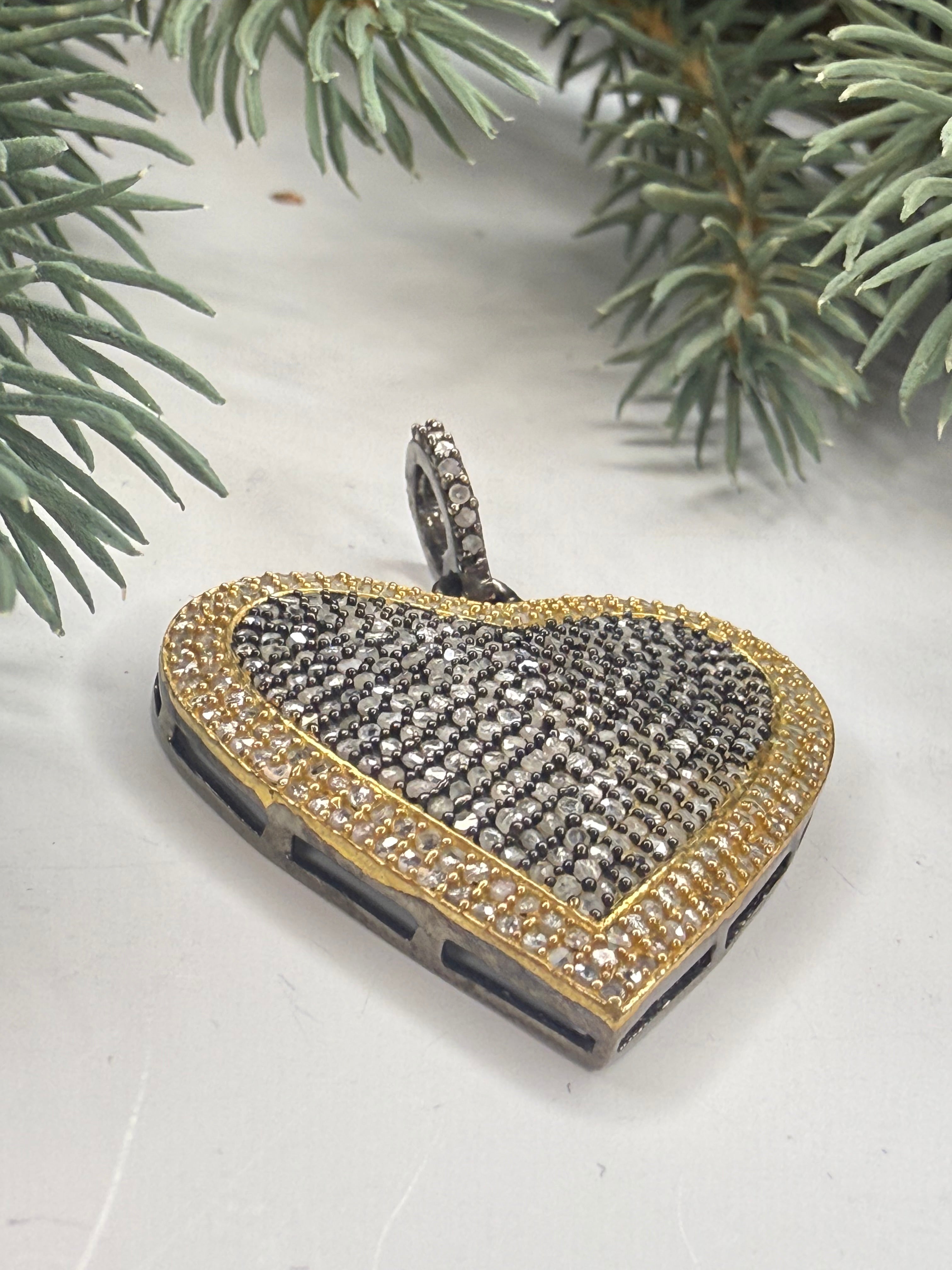 Heart shaped gold and silver pendant with pave diamonds on a white background with greenery.