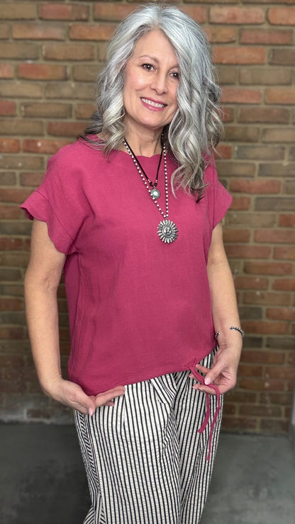 Woman wearing Scalloped Sleeve Tie Hem Top - Berry and striped pants standing against a brick wall.