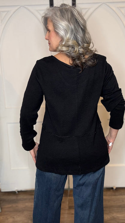 Woman wearing The Black Wanda Top layered with the Silver Snake and Gold Paperclip Chain Necklace, the Silver Snake and Gold Paperclip Chain Choker Necklace and the Gold Cross w/Pearl Necklace  paired with  Judy Blue Palazzo jeans indoors against a white paneled wall.
