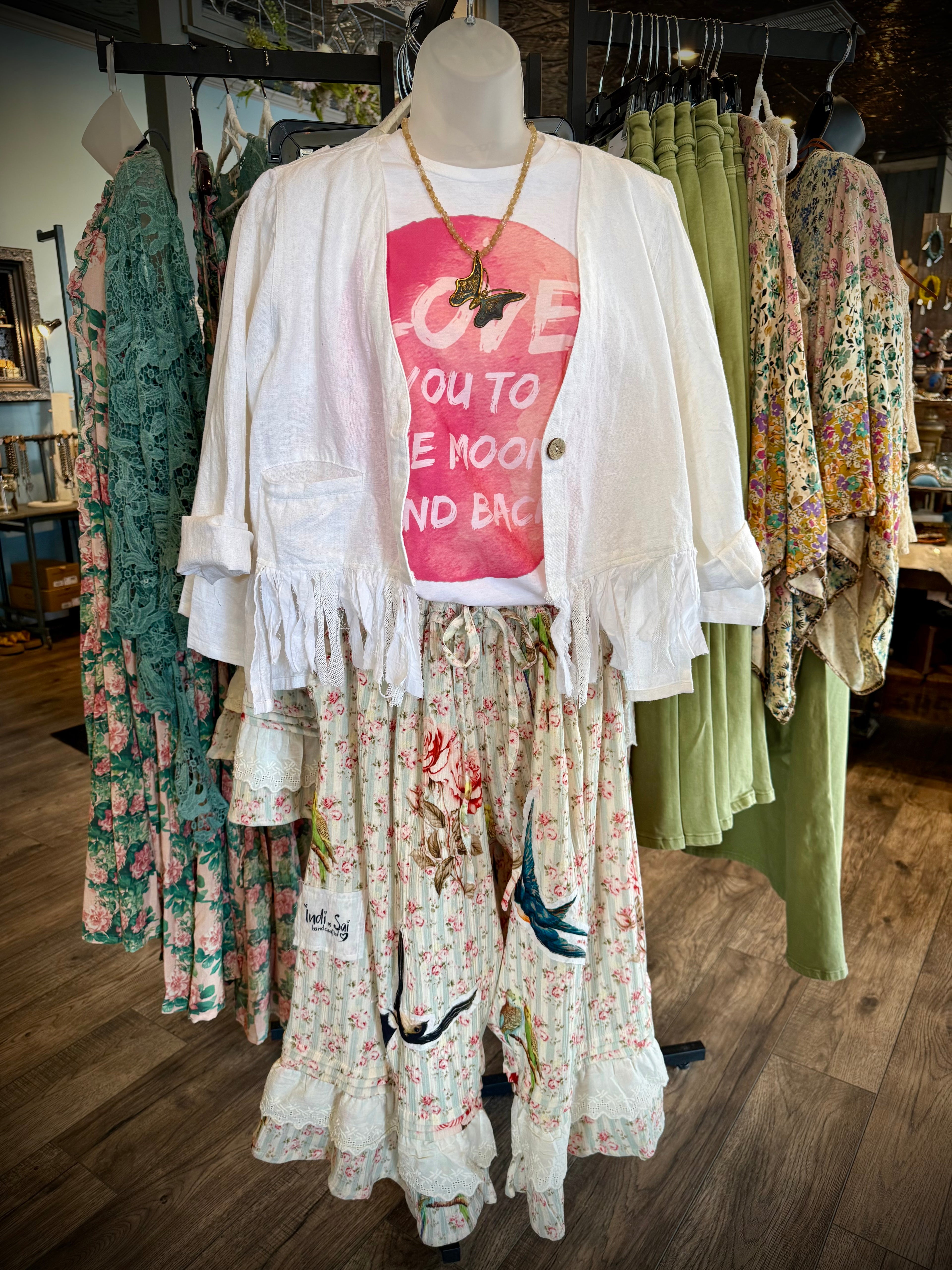 Mannequin wearing a white cardigan over a colorful graphic t-shirt with floral pants in a clothing store.