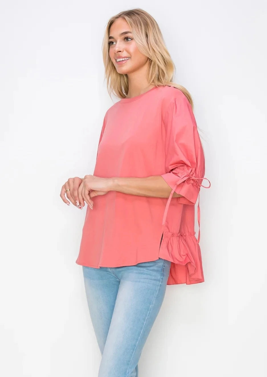 Angled view of Reida Ponte Knit Top in Coral showing ruffled back detail and drawstring tie sleeve detail.