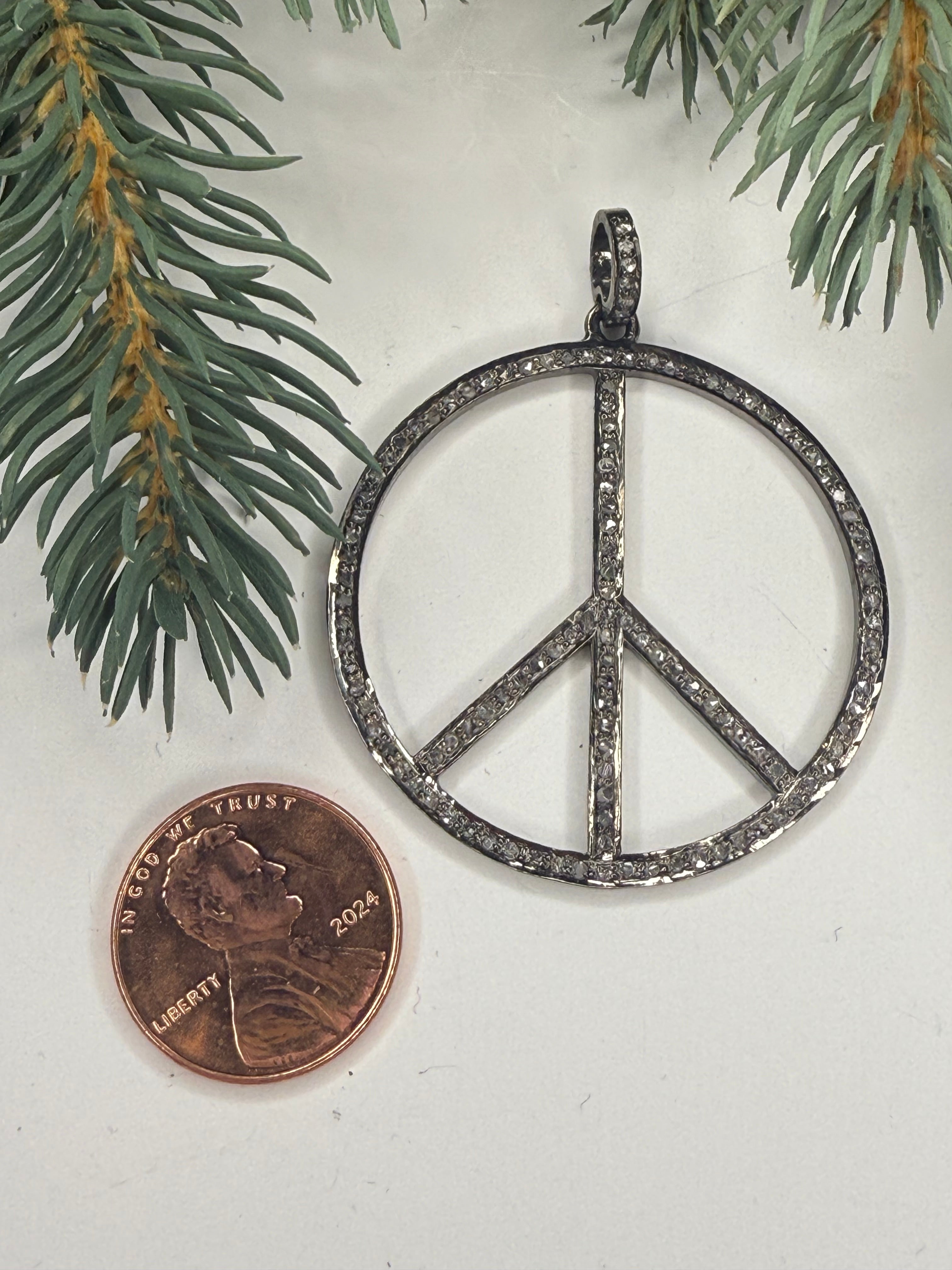 Silver peace symbol pendant next to a penny on a white background with greenery