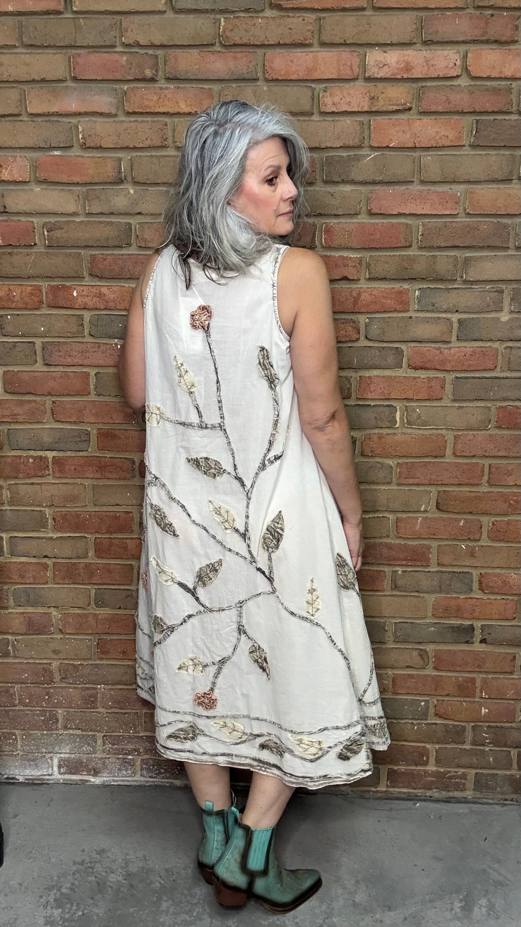 Woman wearing a white dress with floral patterns against a brick wall.