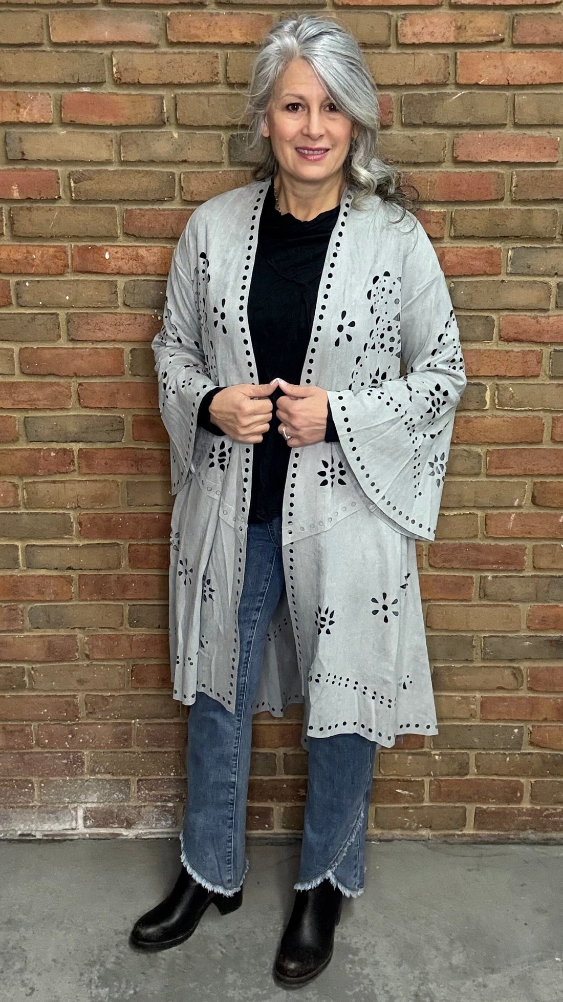 Woman wearing the Grey Suede Laser Cut Jacket standing against a brick wall.