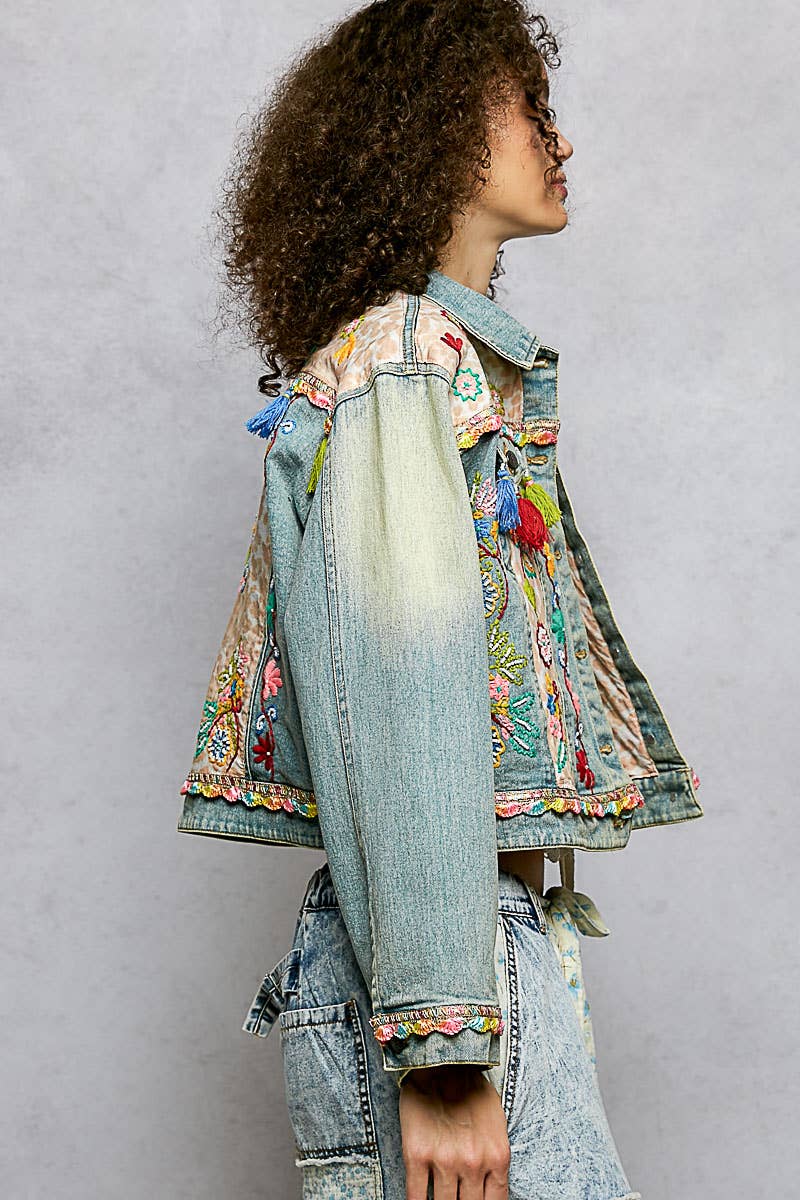 Person wearing a denim jacket with colorful floral embroidery on a plain background