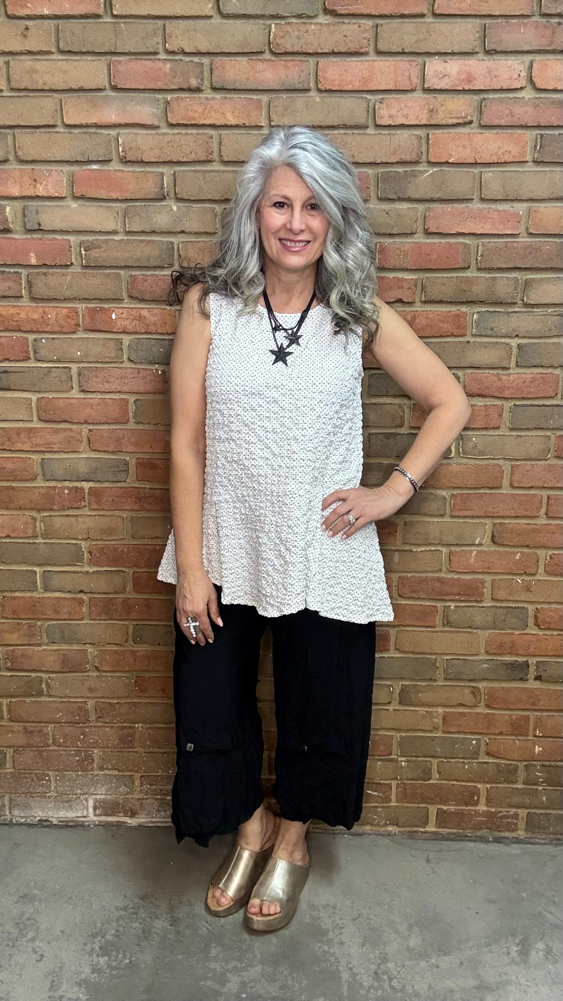 Woman wearing Lyndon Tank - Polka Dot and black pants against a brick wall.