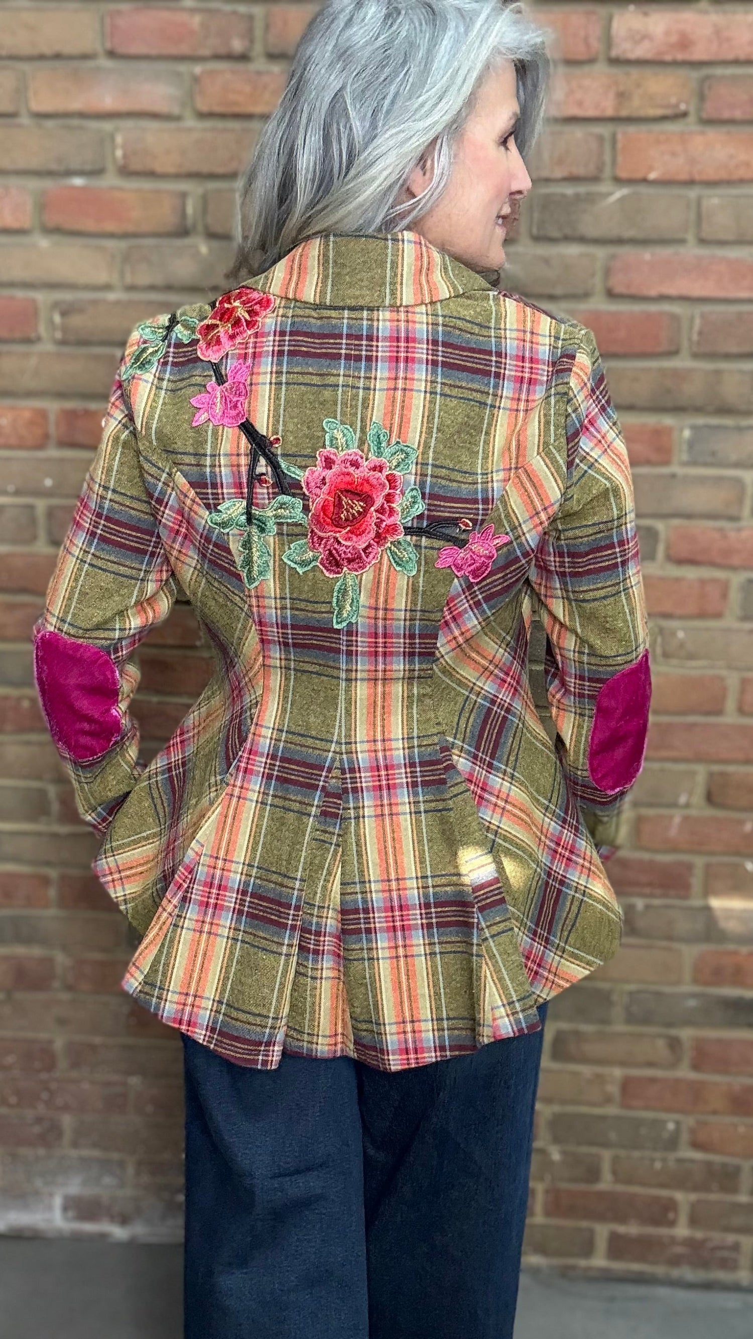 Person wearing a plaid jacket with floral embellishments against a brick wall.