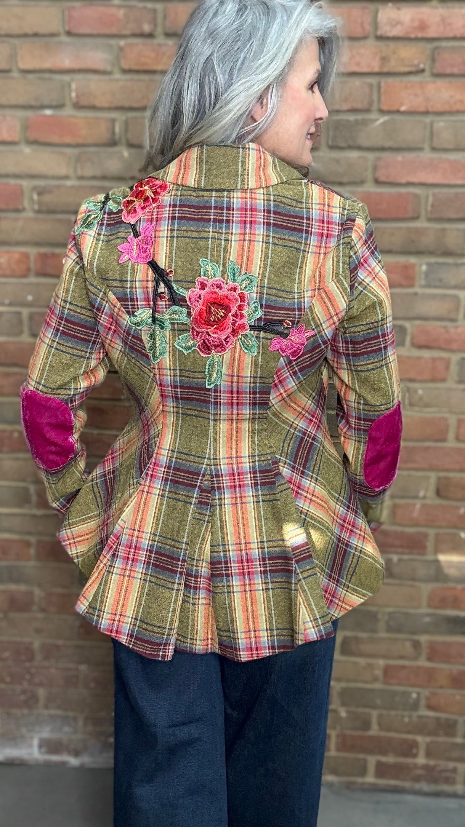 Person wearing a plaid jacket with floral embellishments against a brick wall.