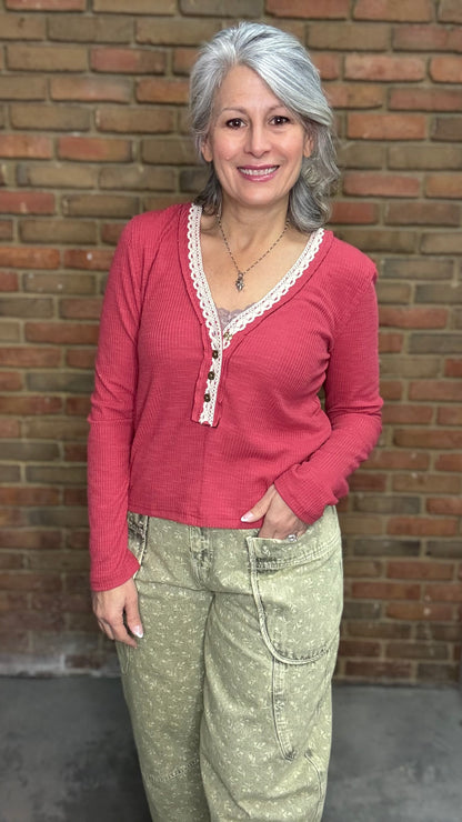 Person wearing the Raspberry Rose Ribbed Henley long-sleeve Top with the Floral Printed Barrel Pants against a brick wall.