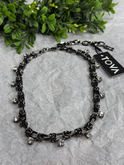 Black chain necklace with decorative elements on a gray surface with greenery