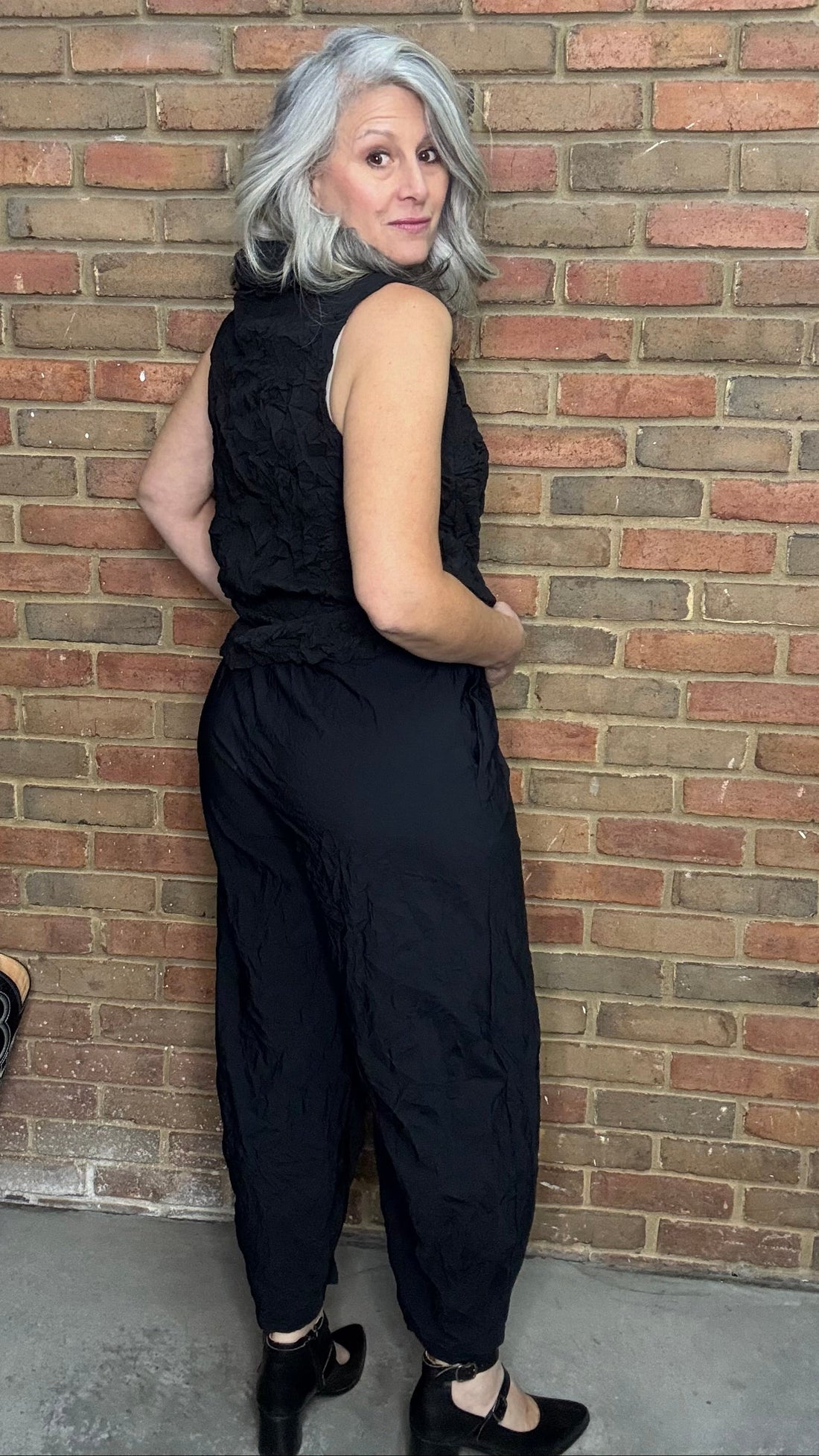 Person wearing a black sleeveless top and pants against a brick wall.