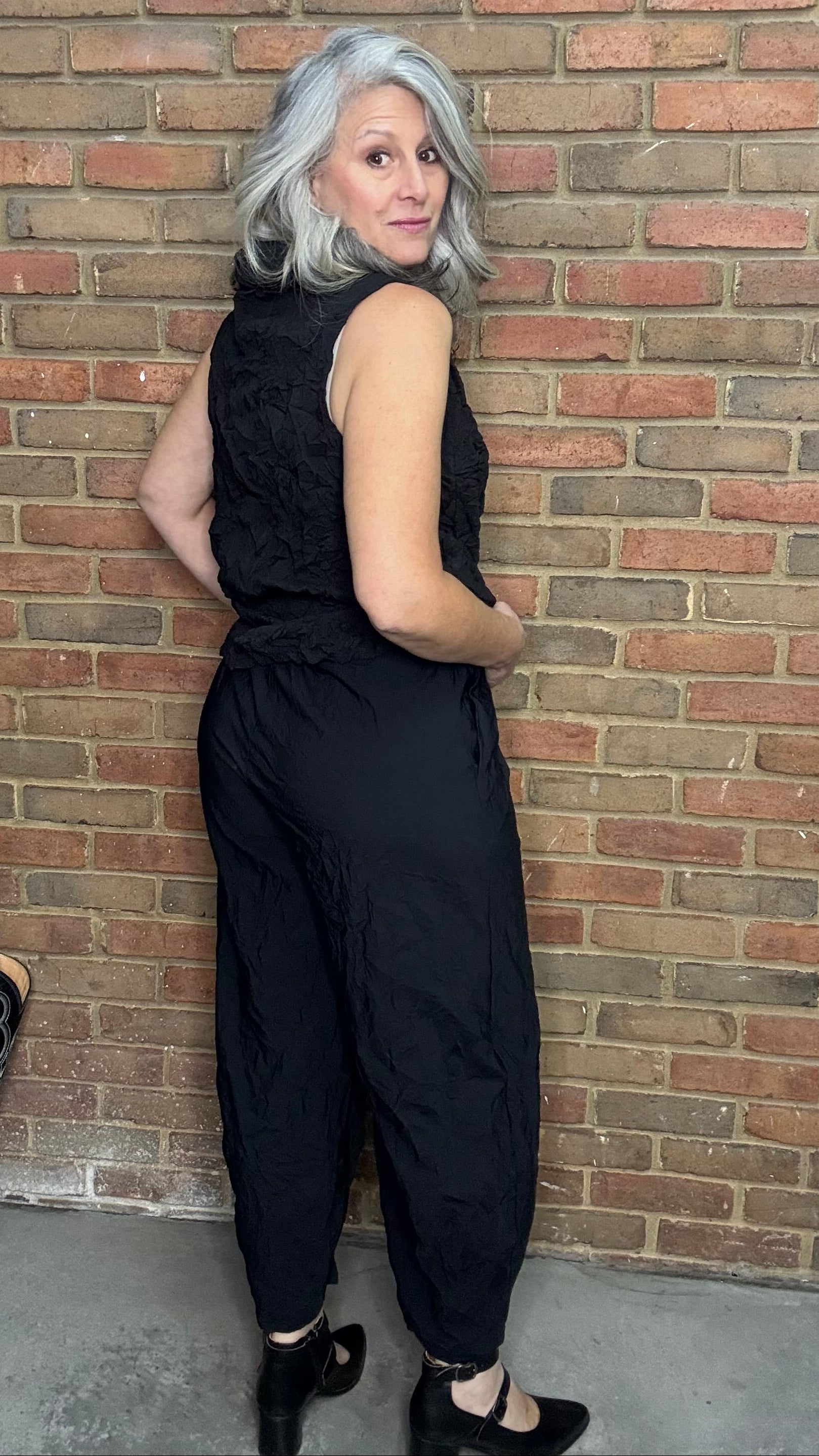Person wearing a black sleeveless top and pants against a brick wall.