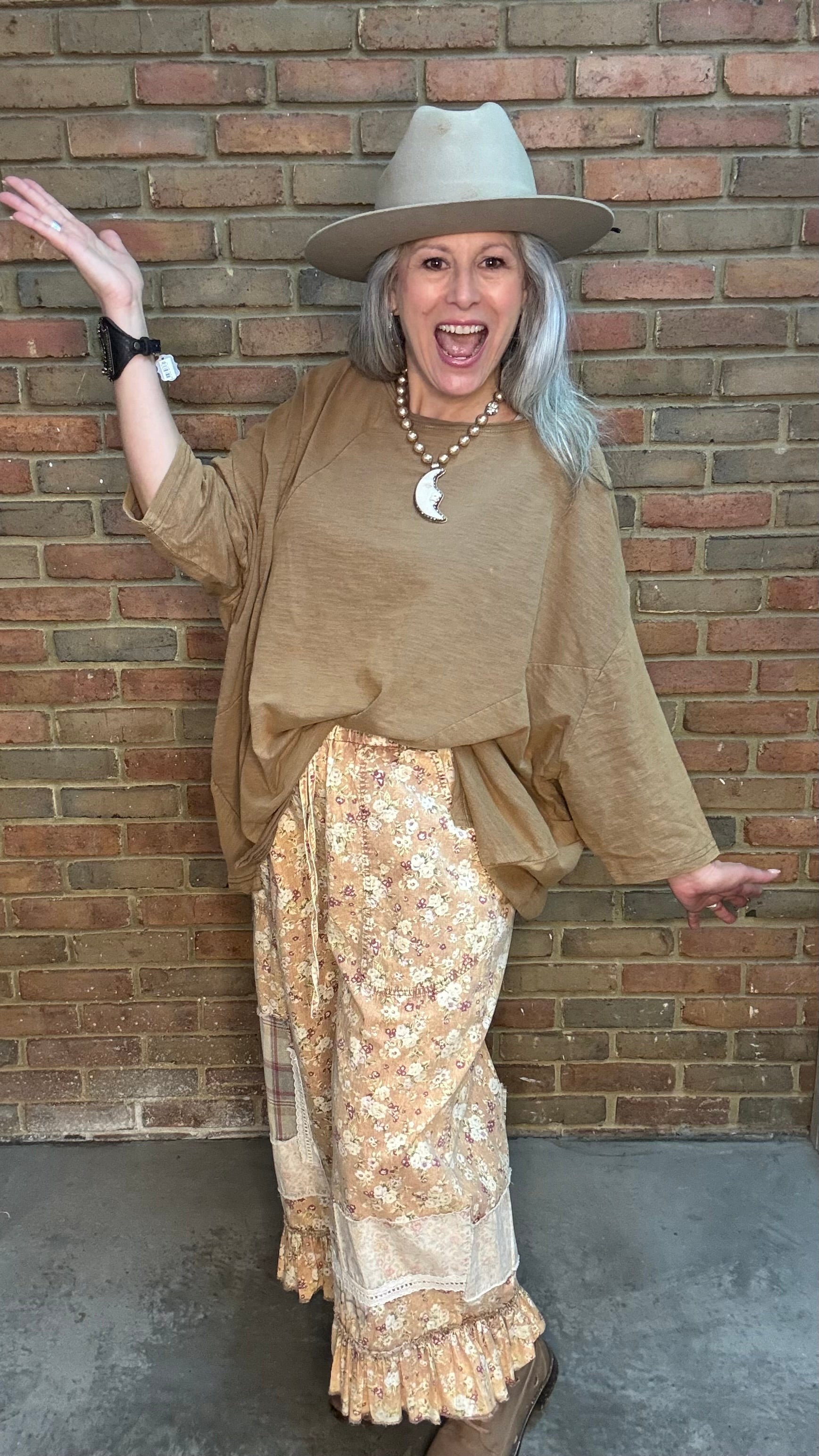 Woman wearing Be Free Top - Vintage Latte and patterned pants against a brick wall.