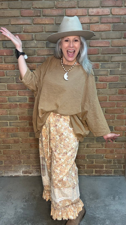 Woman wearing Be Free Top - Vintage Latte and patterned pants against a brick wall.