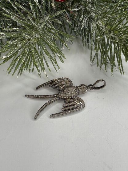 Bird shaped pendant in pave diamonds on a white surface with a Christmas tree branch in the background.