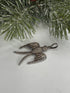 Bird shaped pendant in pave diamonds on a white surface with a Christmas tree branch in the background.