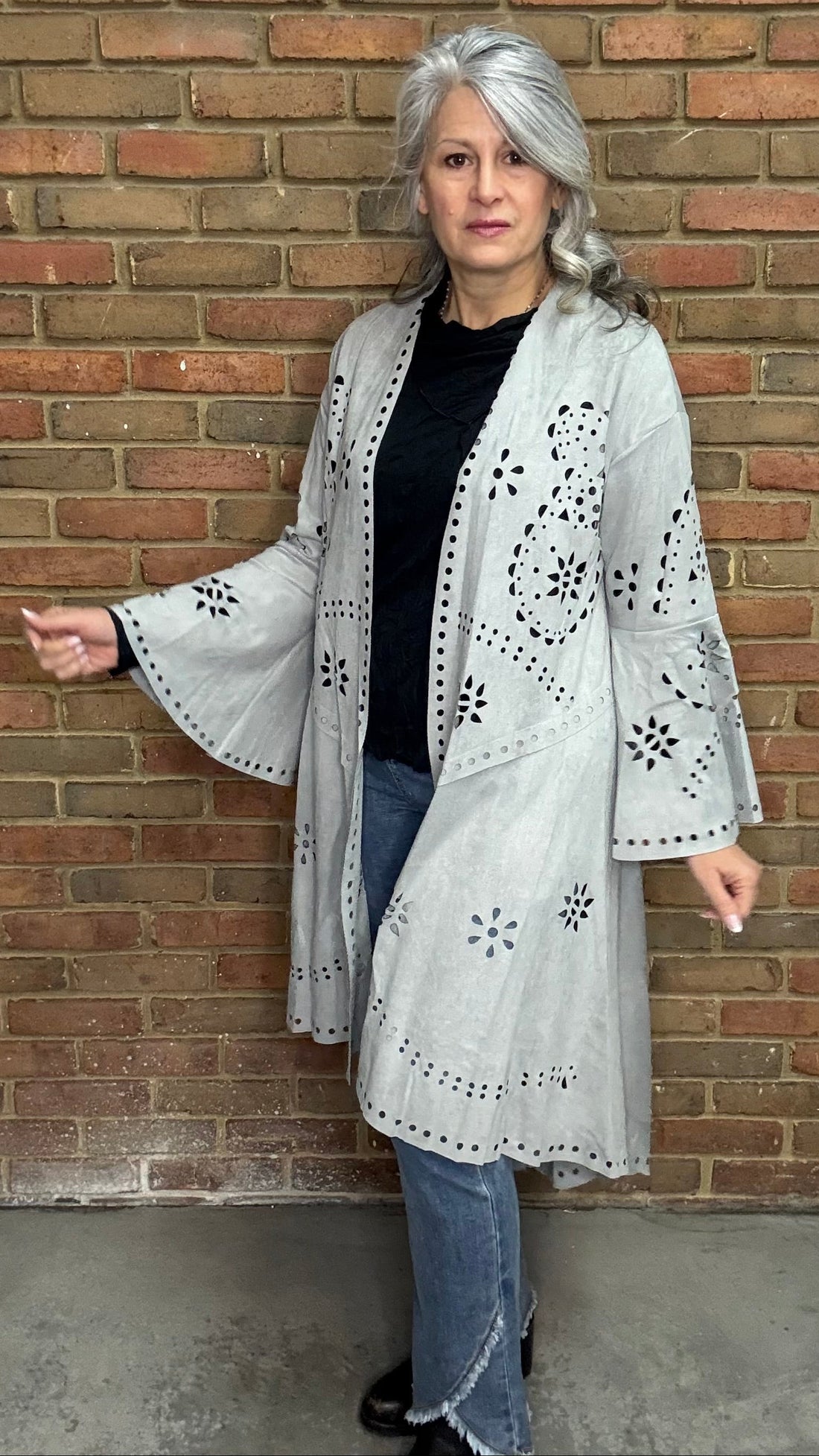 Woman wearing the Grey Suede Laser Cut Jacket standing against a brick wall.