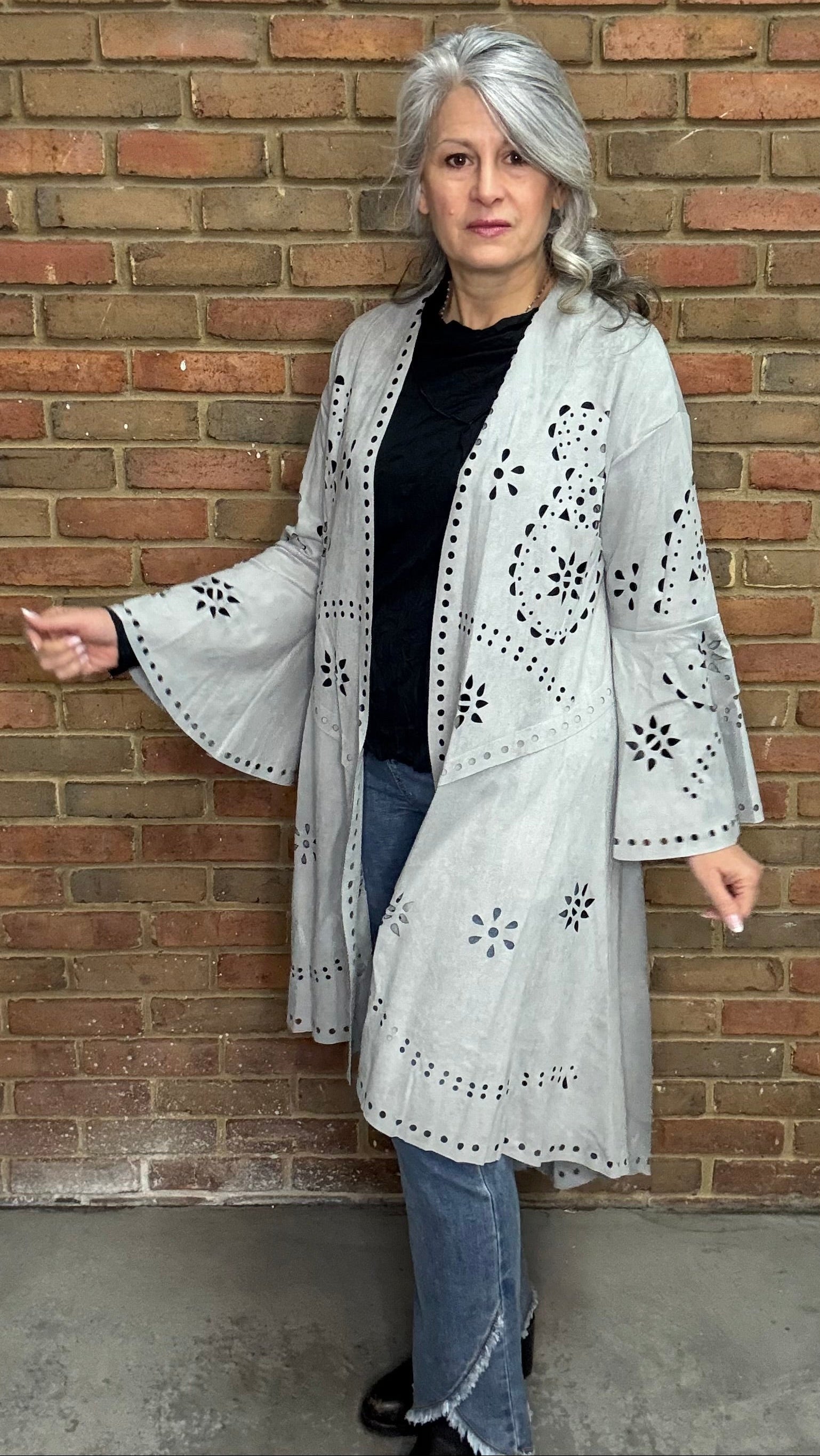 Woman wearing the Grey Suede Laser Cut Jacket standing against a brick wall.
