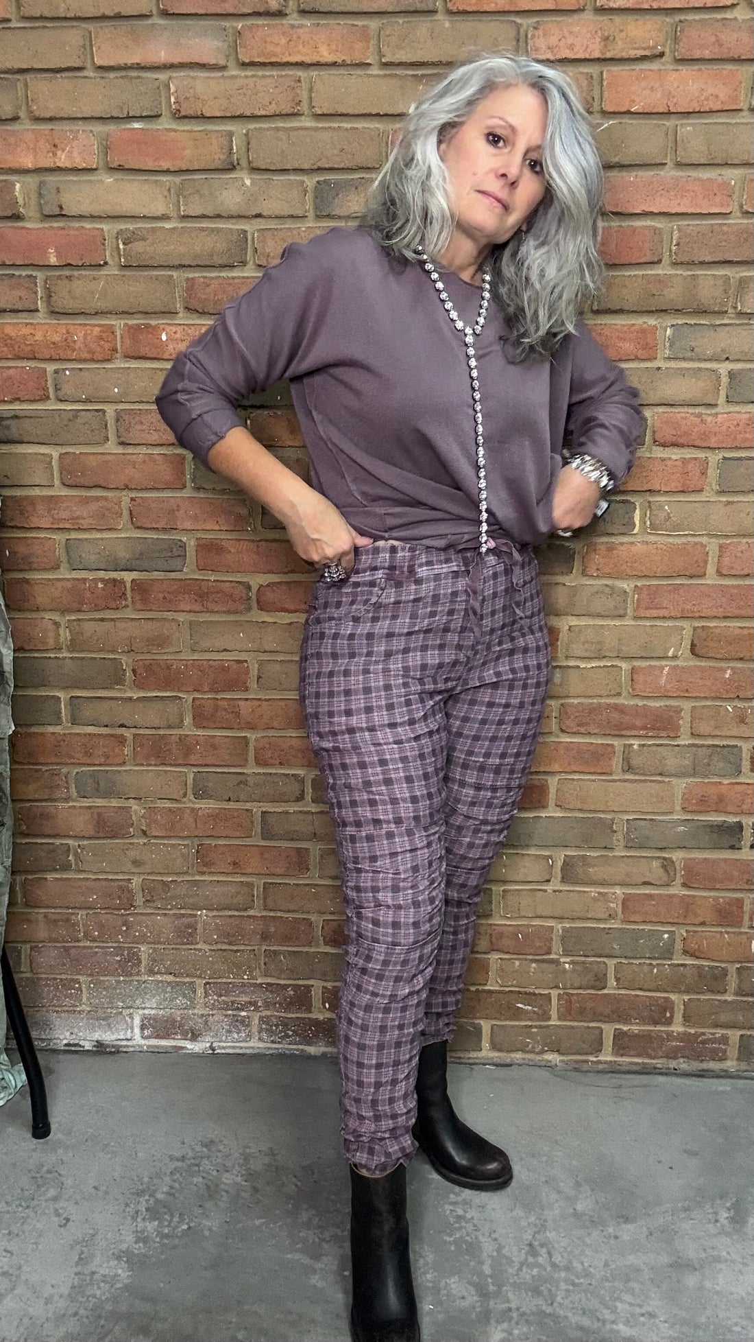 Person wearing a purple outfit with plaid pants against a brick wall.