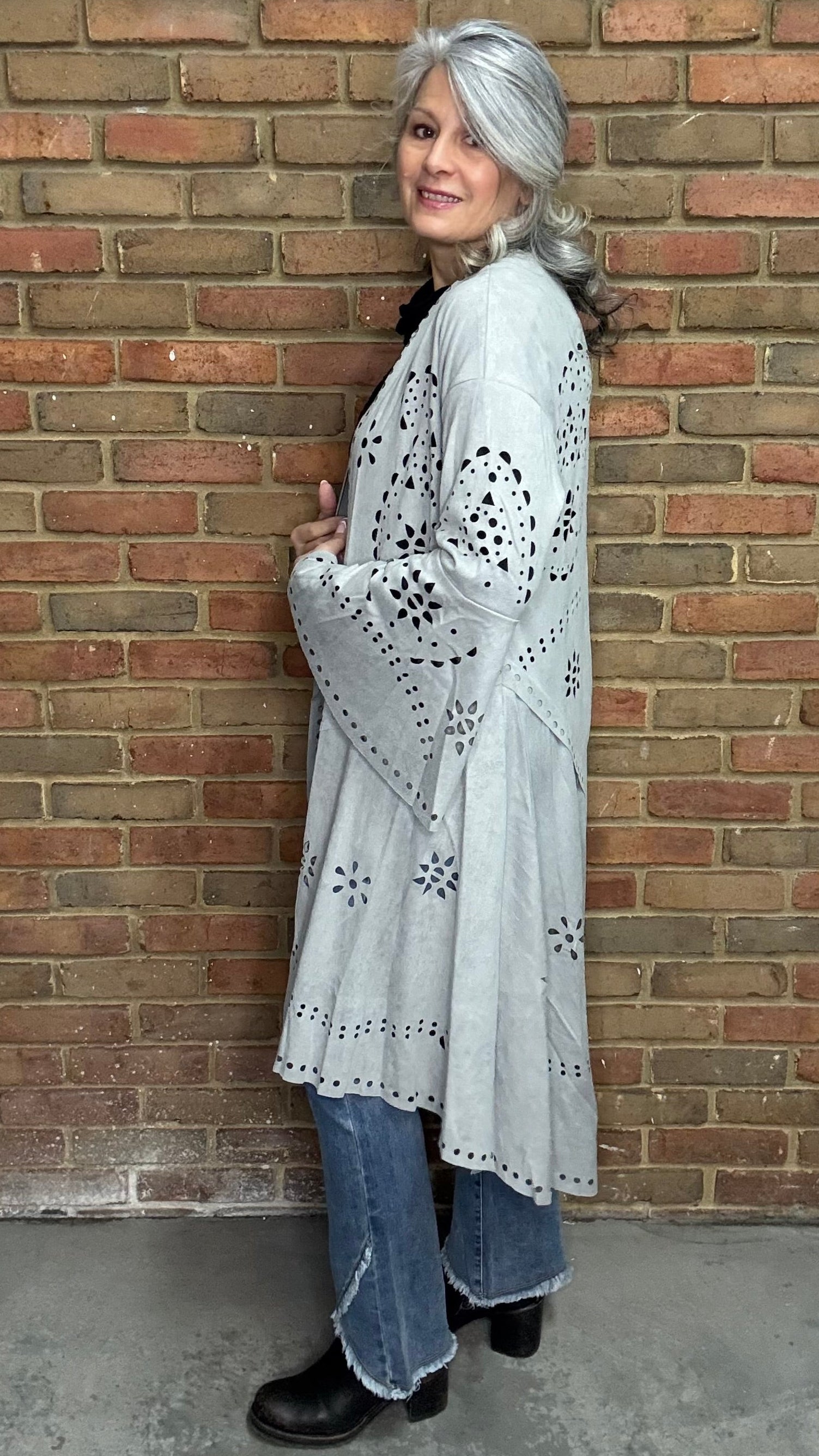 Woman wearing the Grey Suede Laser Cut Jacket standing against a brick wall.