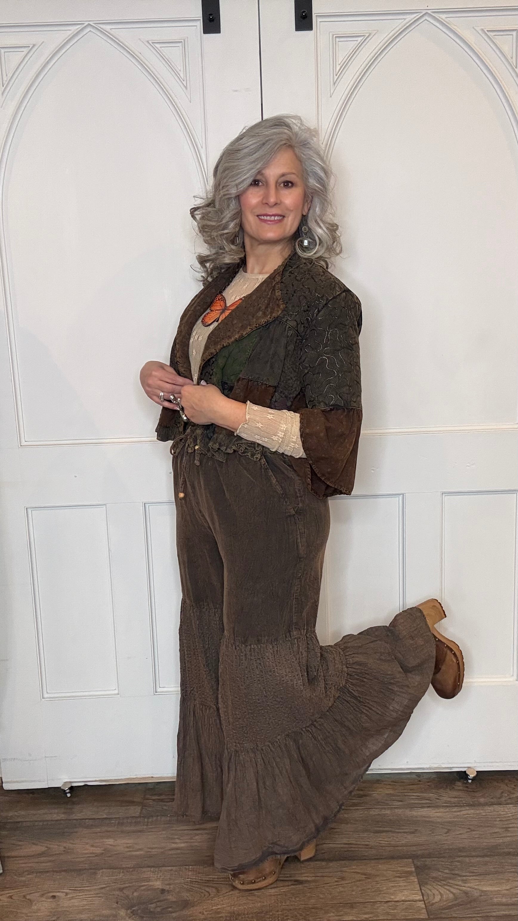 Woman wearing Boho Embroidered Lapel Crop Jacket, beige lace top with Monarch Butterfly Necklace and Amber Boho Chic pants against a white paneled wall.