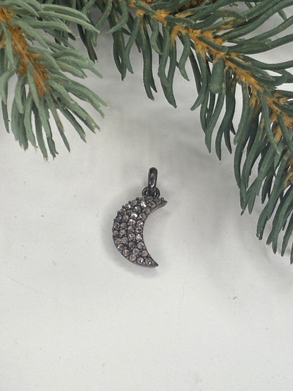 Silver crescent moon charm with diamonds on a white background with a green branch.